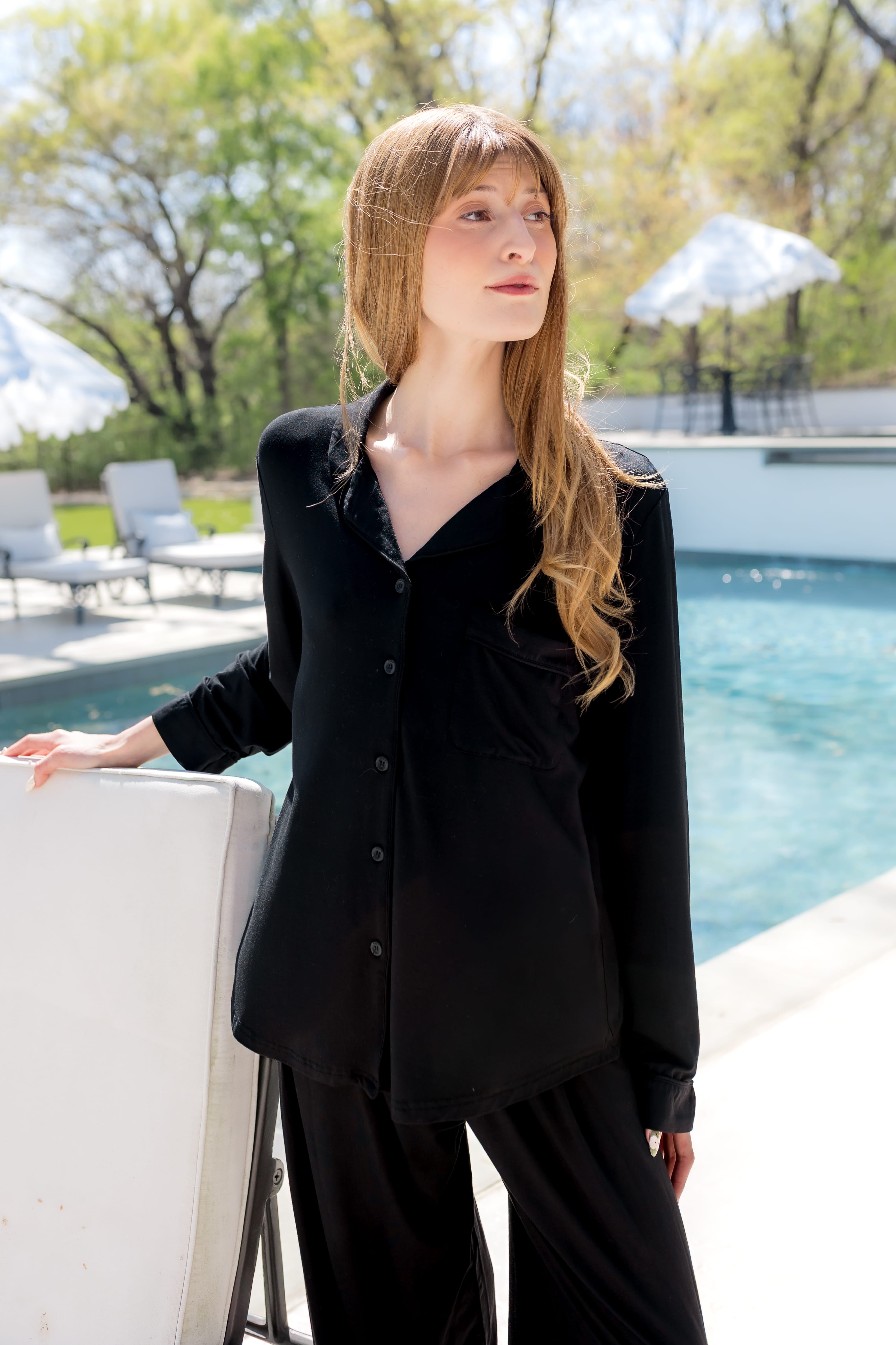 Female model standing by the pool wearing the Long-Sleeved Women's Pajama Set in Midnight with Midnight Trim