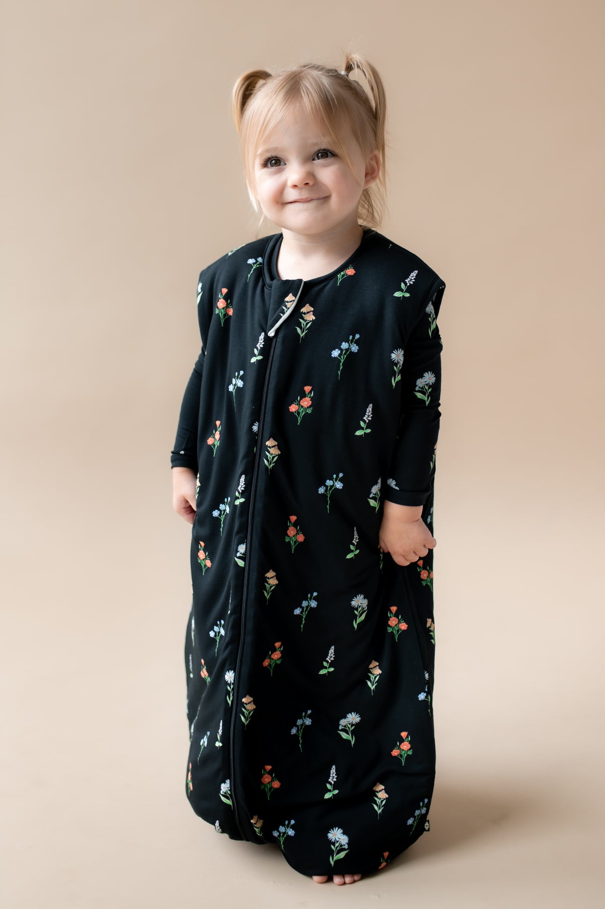 Girl smiling in Sleep Bag Walker in Midnight Wildflower 2.5 print on a beige background