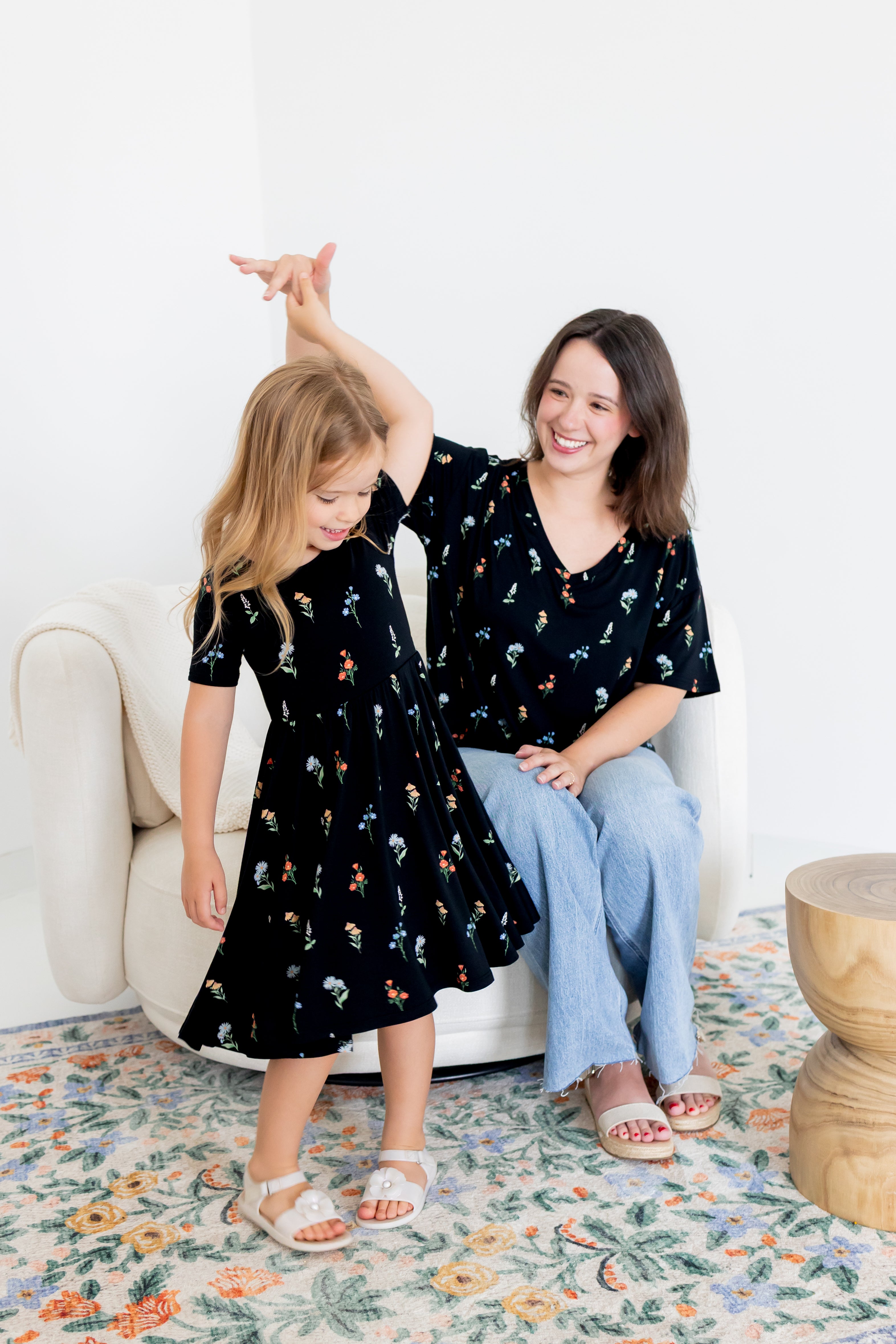 Girl twirling in Twirl Dress in Midnight Wildflower print with a model wearing Women's Relaxed Fit V-Neck in similar print over blue jeans