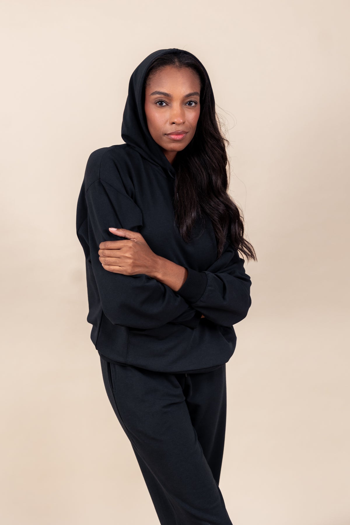 Woman wearing Women's Hoodie in Midnight color with crossed hands over similar color women's jogger pants on a beige background