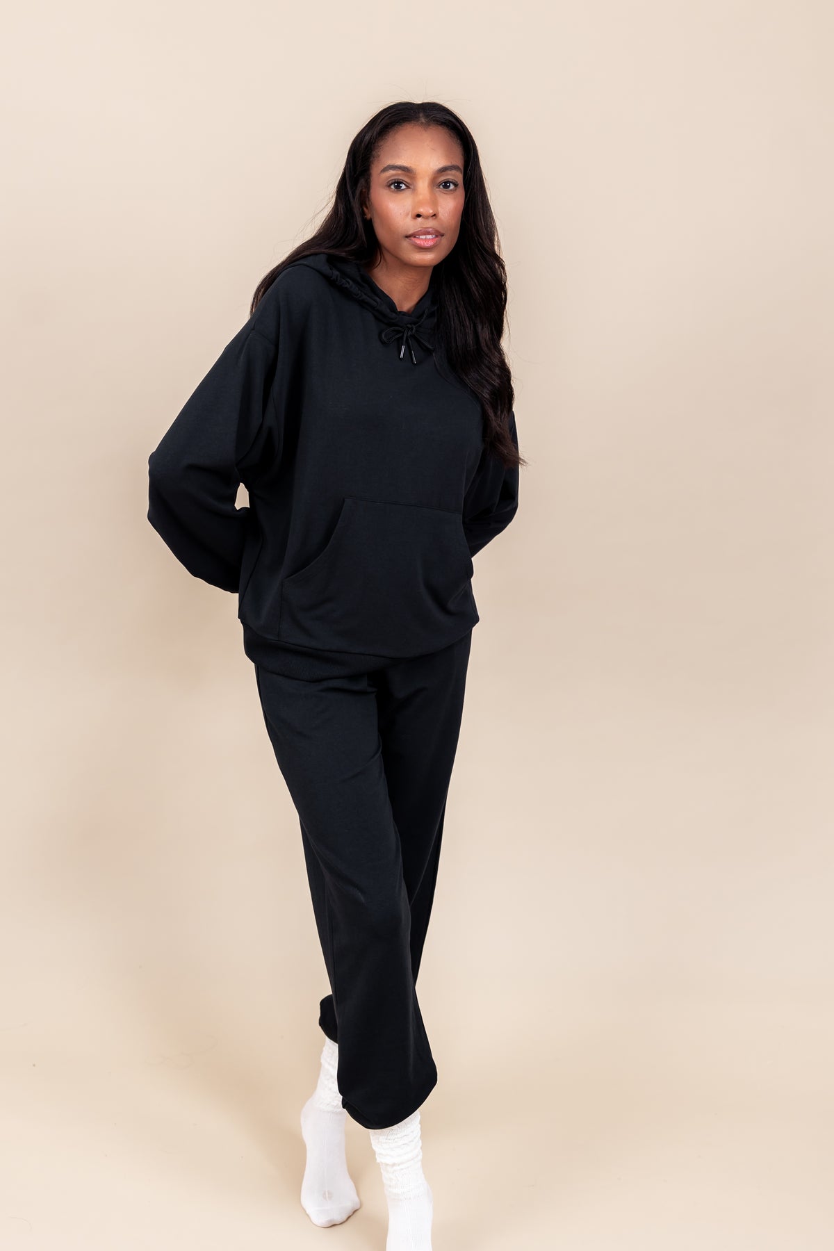 Woman wearing Women's Hoodie in Midnight color over similar color women's jogger pants and white socks on a beige background
