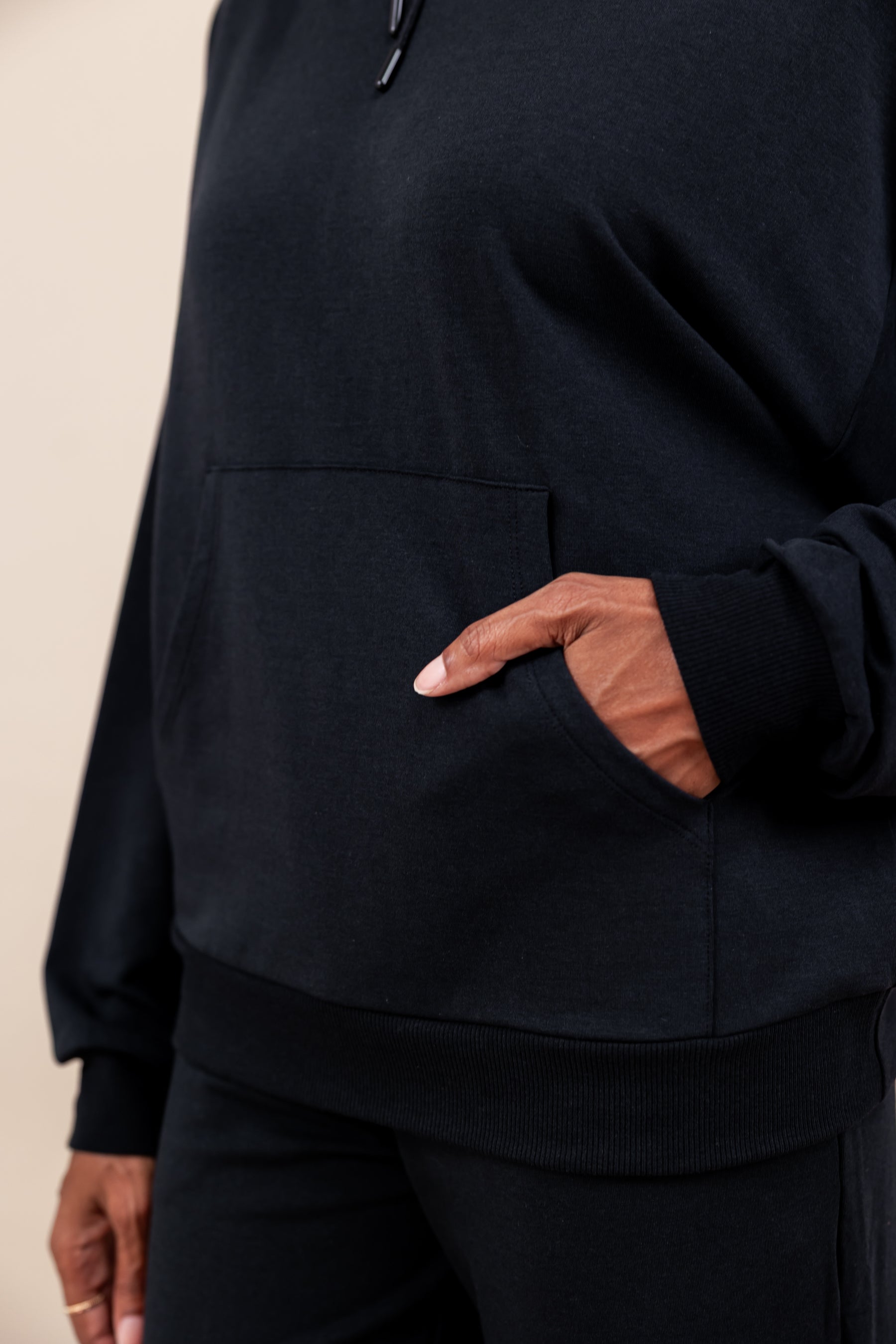 Close up of Woman wearing Women's Hoodie in Midnight color with pockets over similar color women's jogger pants on a beige background