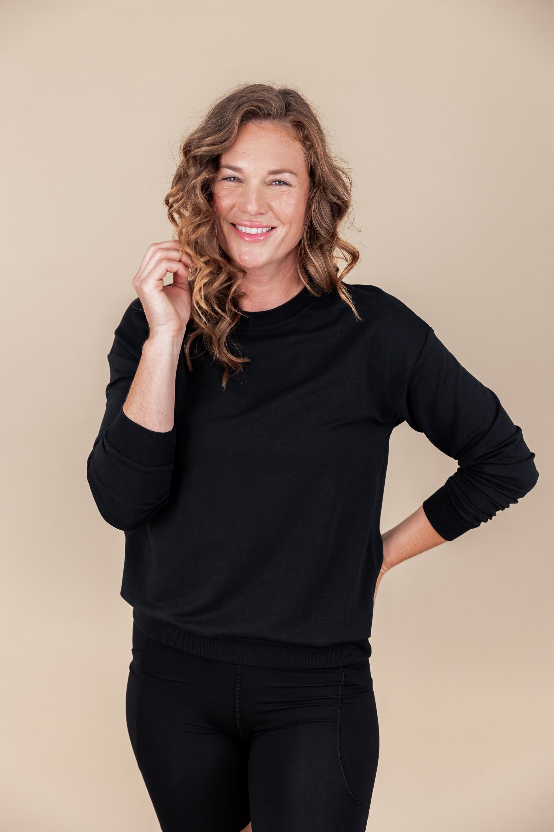 Woman wearing Women's Sweatshirt in Midnight color over black shorts on a beige background