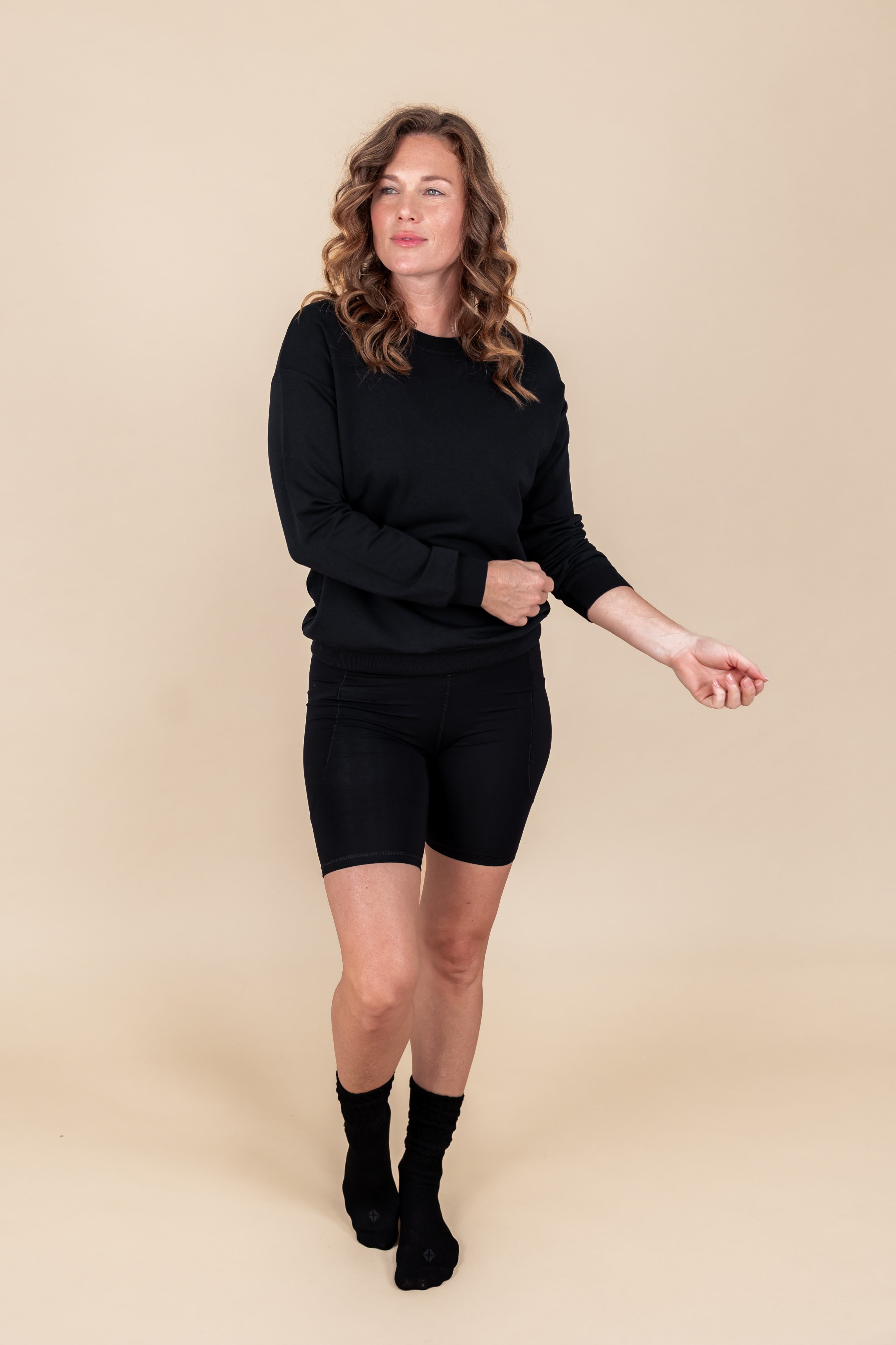 Woman wearing Women's Sweatshirt in Midnight color over black shorts and socks on a beige background