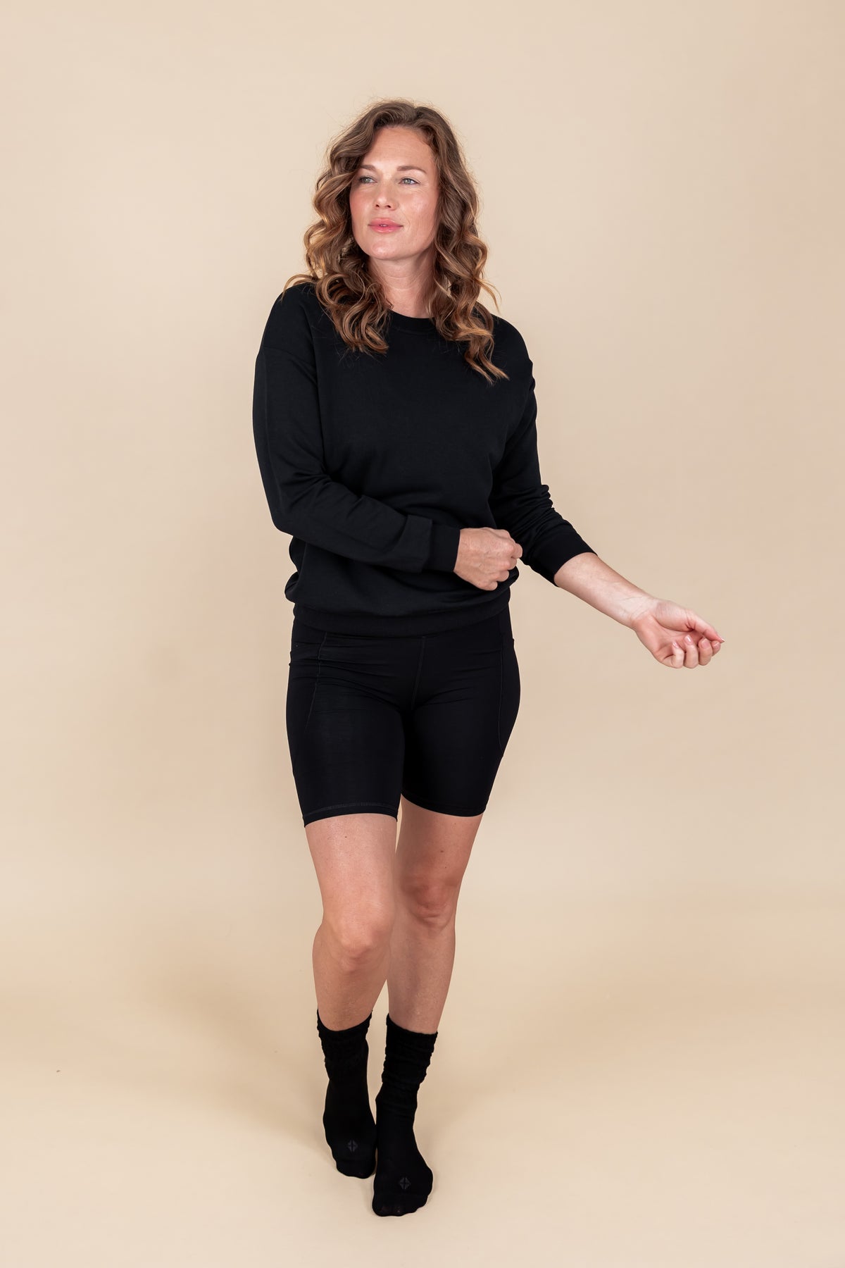 Woman wearing Women's Sweatshirt in Midnight color over black shorts and socks on a beige background