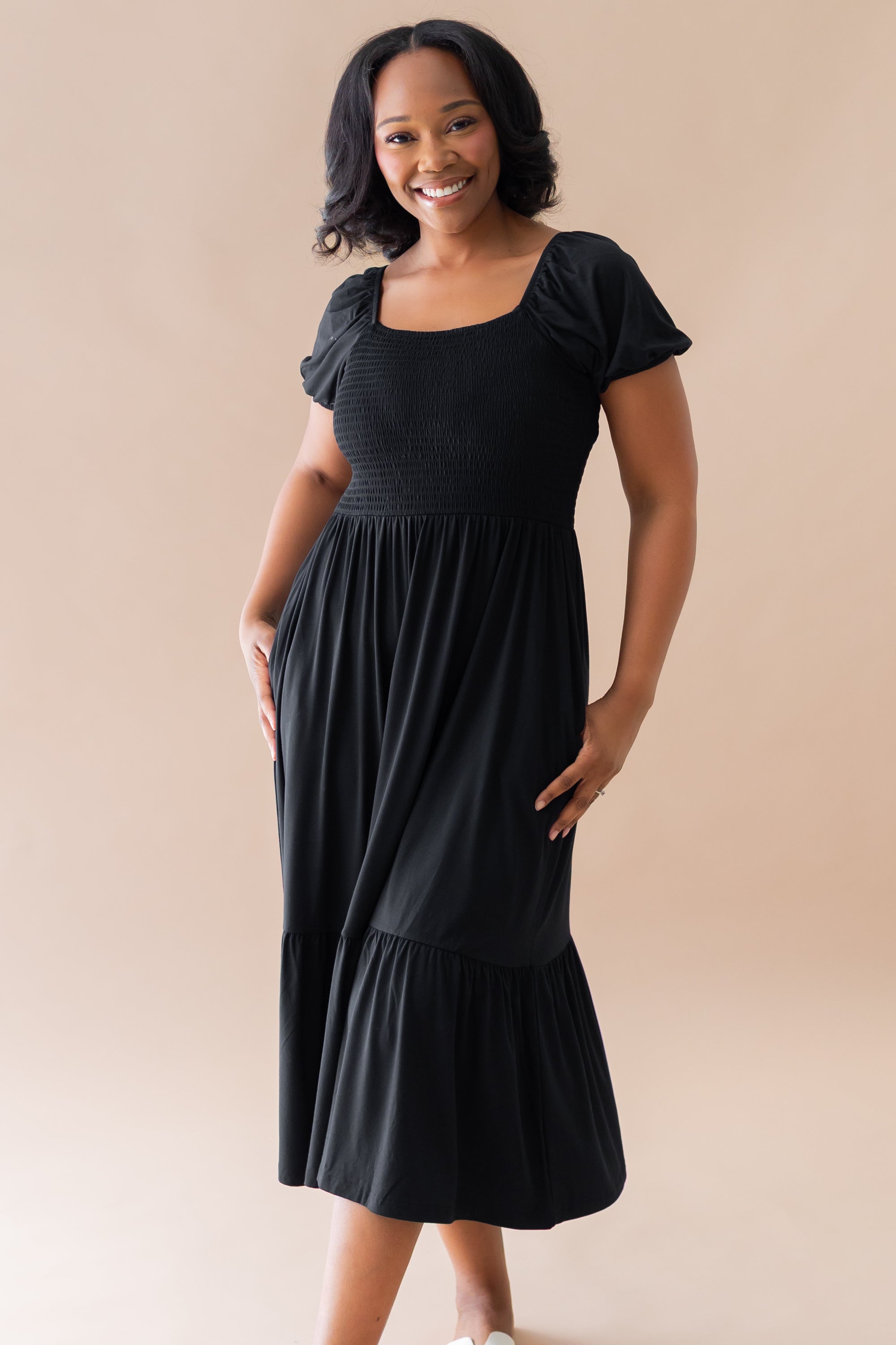 Female model posing wearing the Women’s Smocked Dress in Midnight in front of a light taupe background