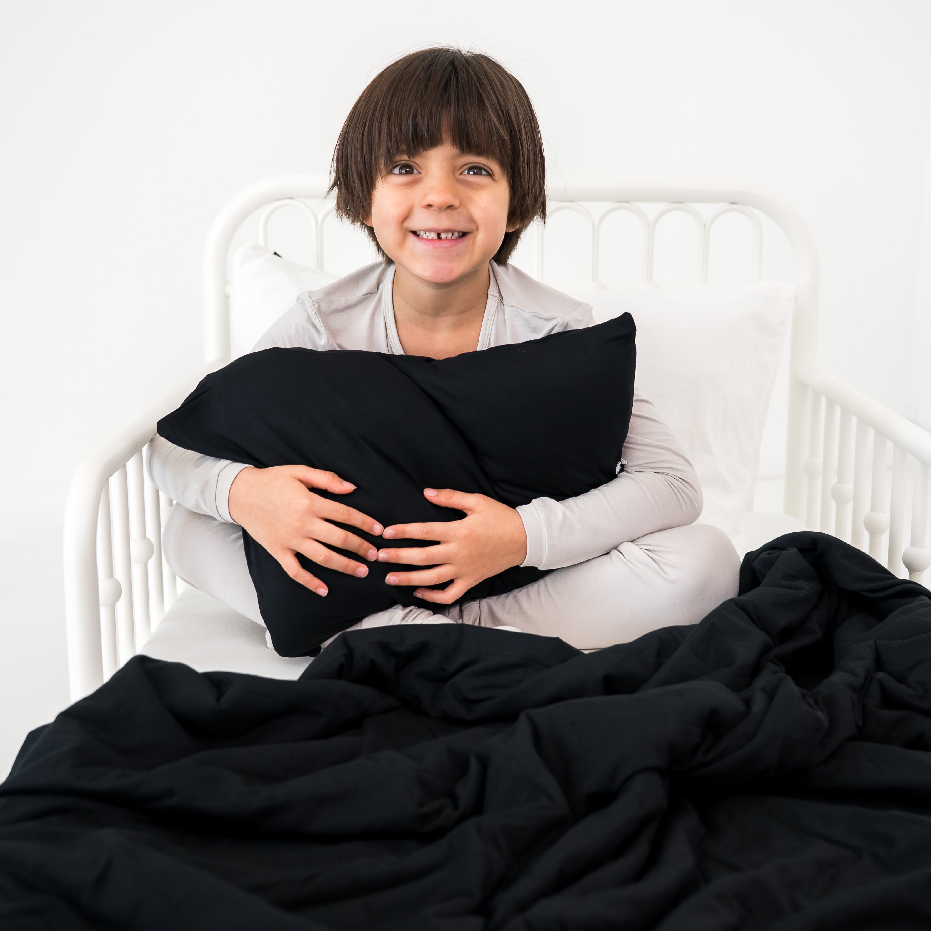 Child holding a black pillow on a bed with a black blanket