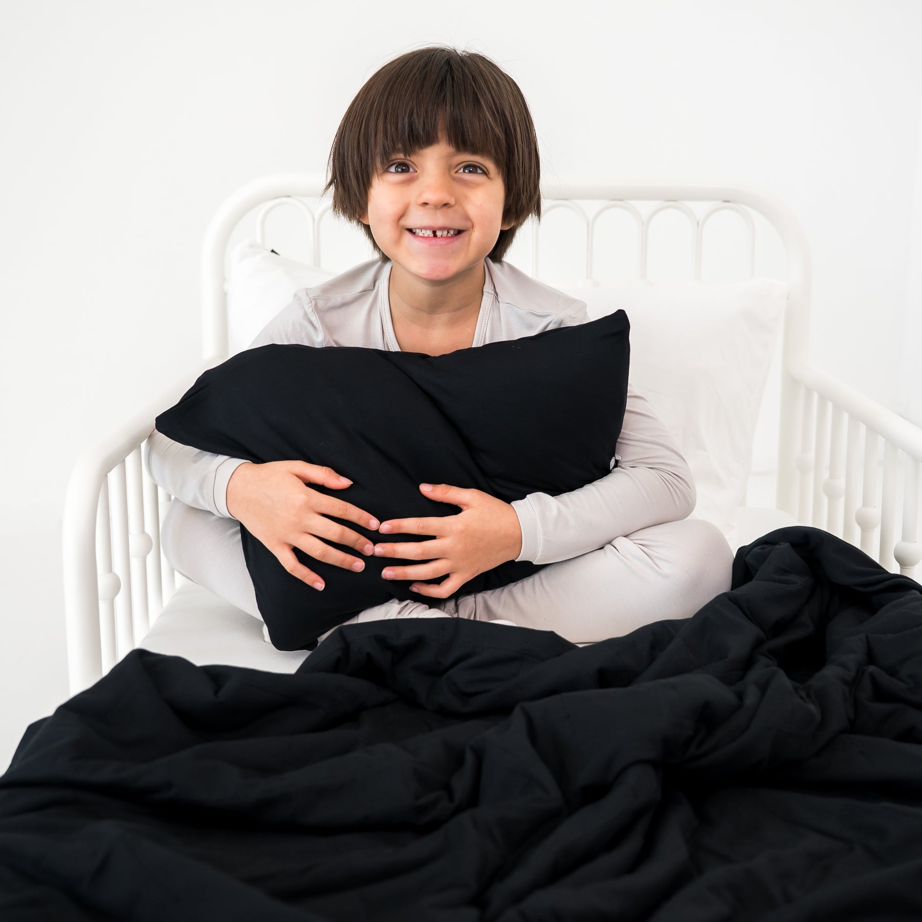 Child holding a black pillow on a bed with a black blanket