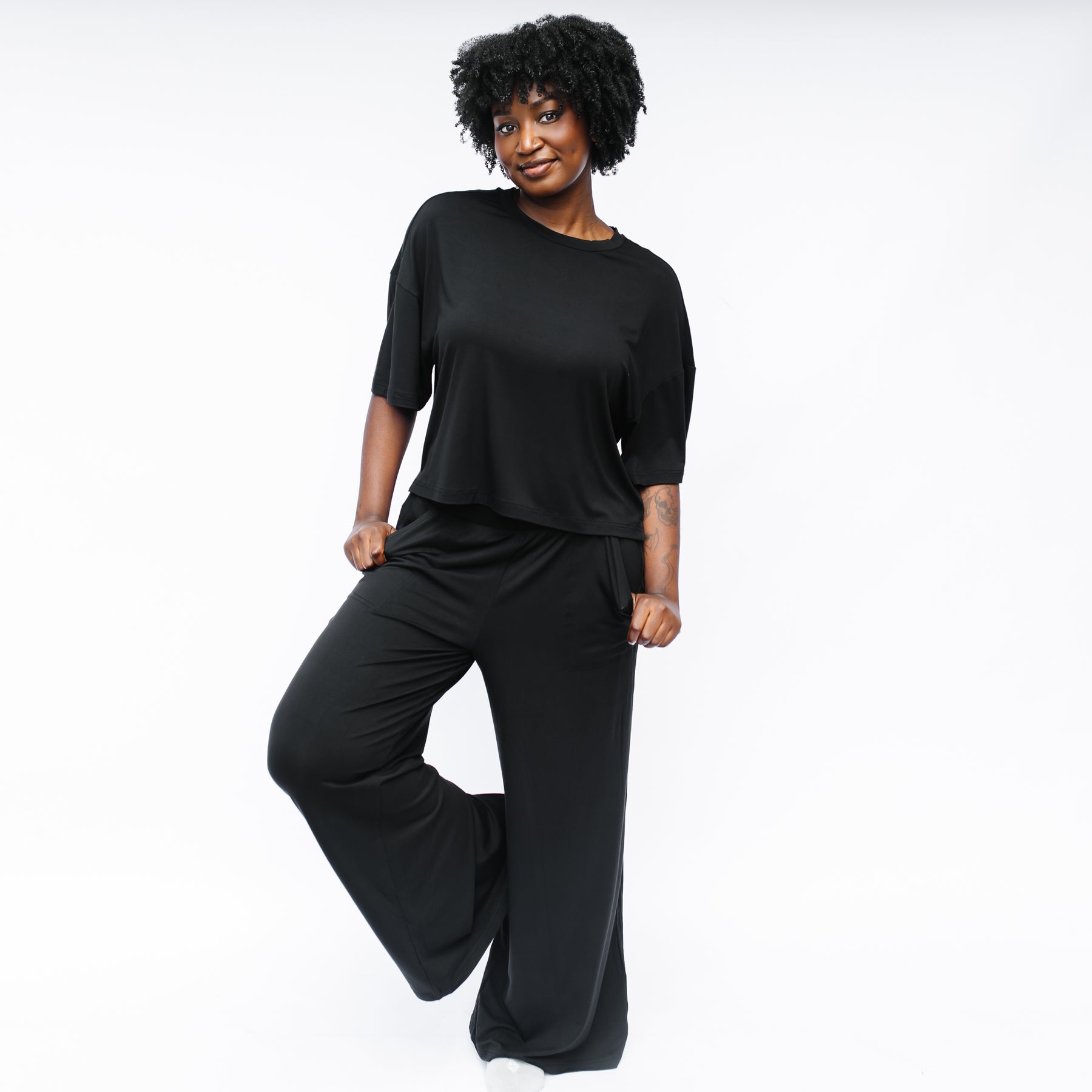 Female model standing in front of a white background wearing the Women's Short Sleeve Tee in Midnight with wide leg pants