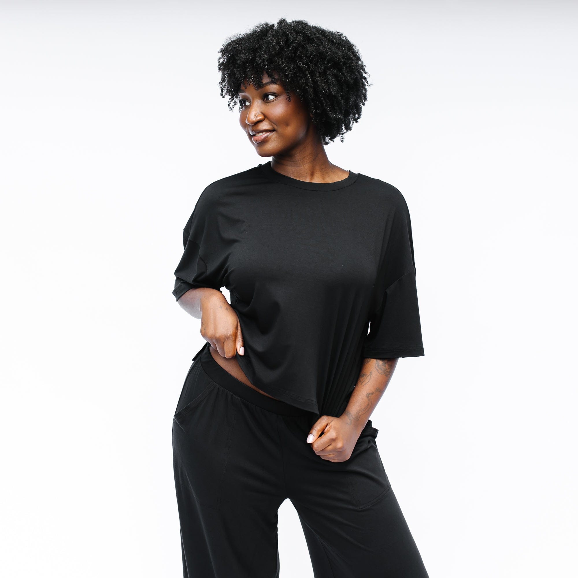 Female model standing in front of a white backdrop looking off to the side wearing the Women's Short Sleeve Tee in Midnight with matching wide leg pants