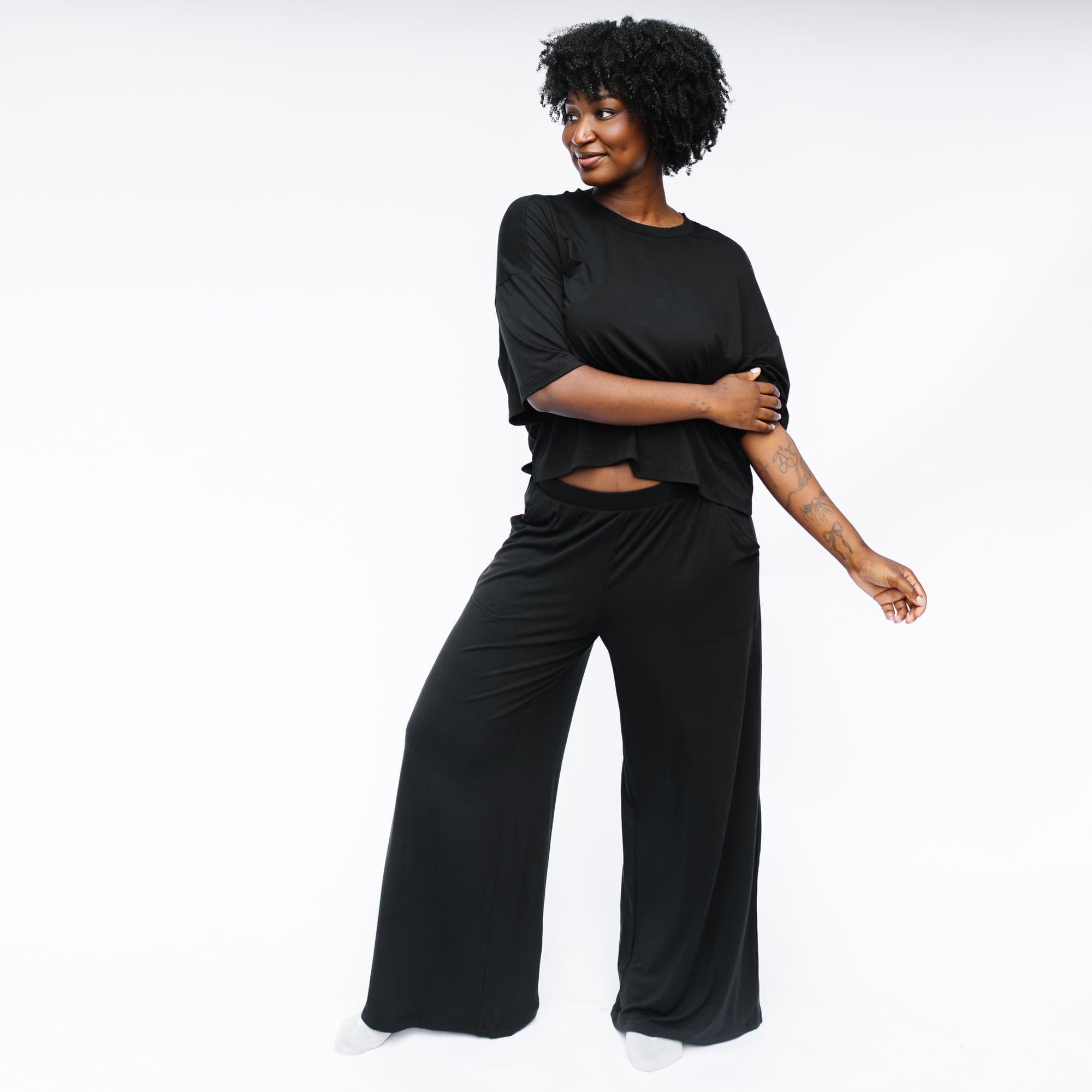 Female model standing in front of a white background wearing the Women's Wide Leg Pant in Midnight with matching women's short sleeve tee