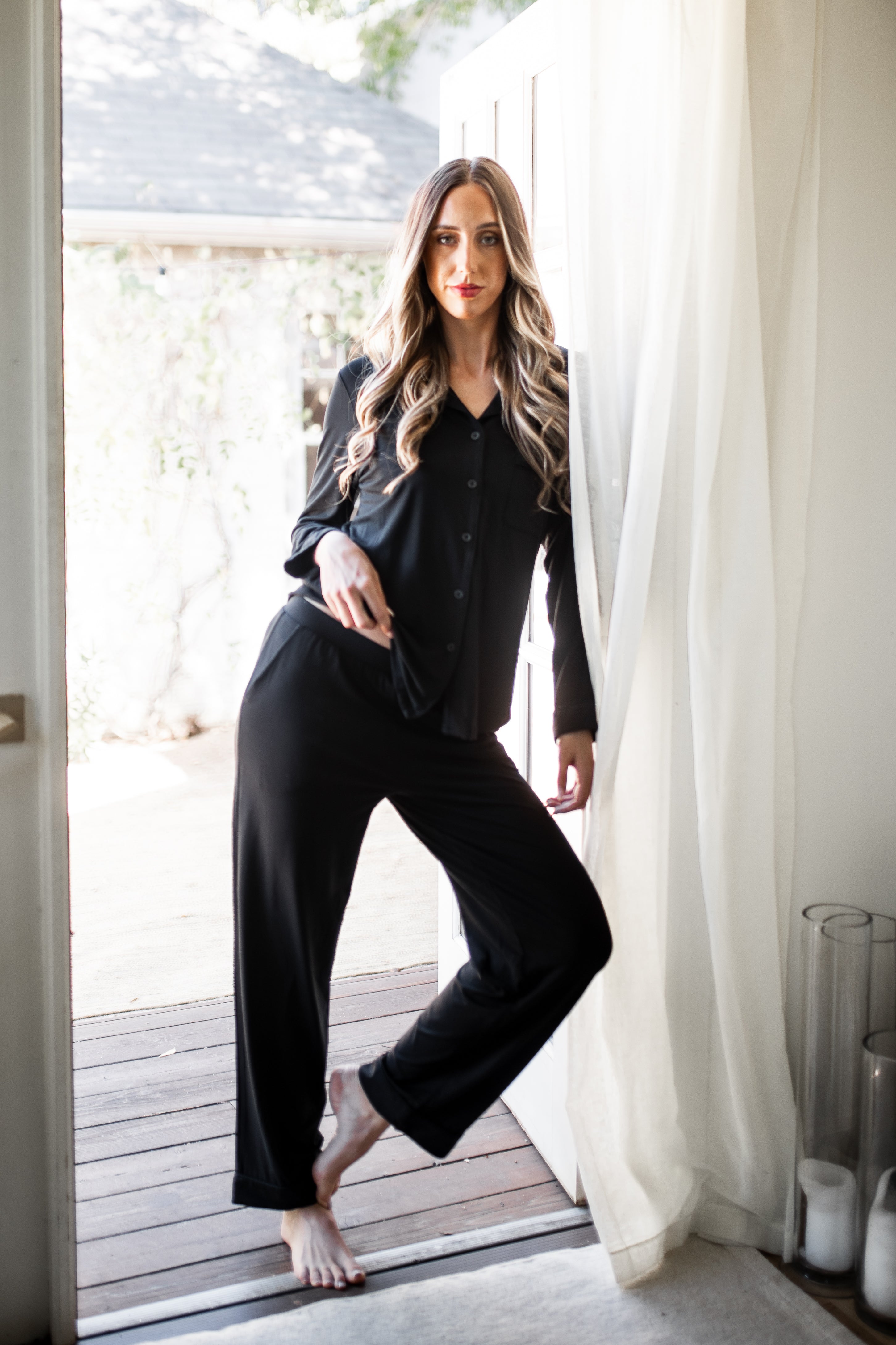Female leaning against a door frame posing wearing the Long-Sleeved Women's Pajama Set in Midnight with Midnight Trim