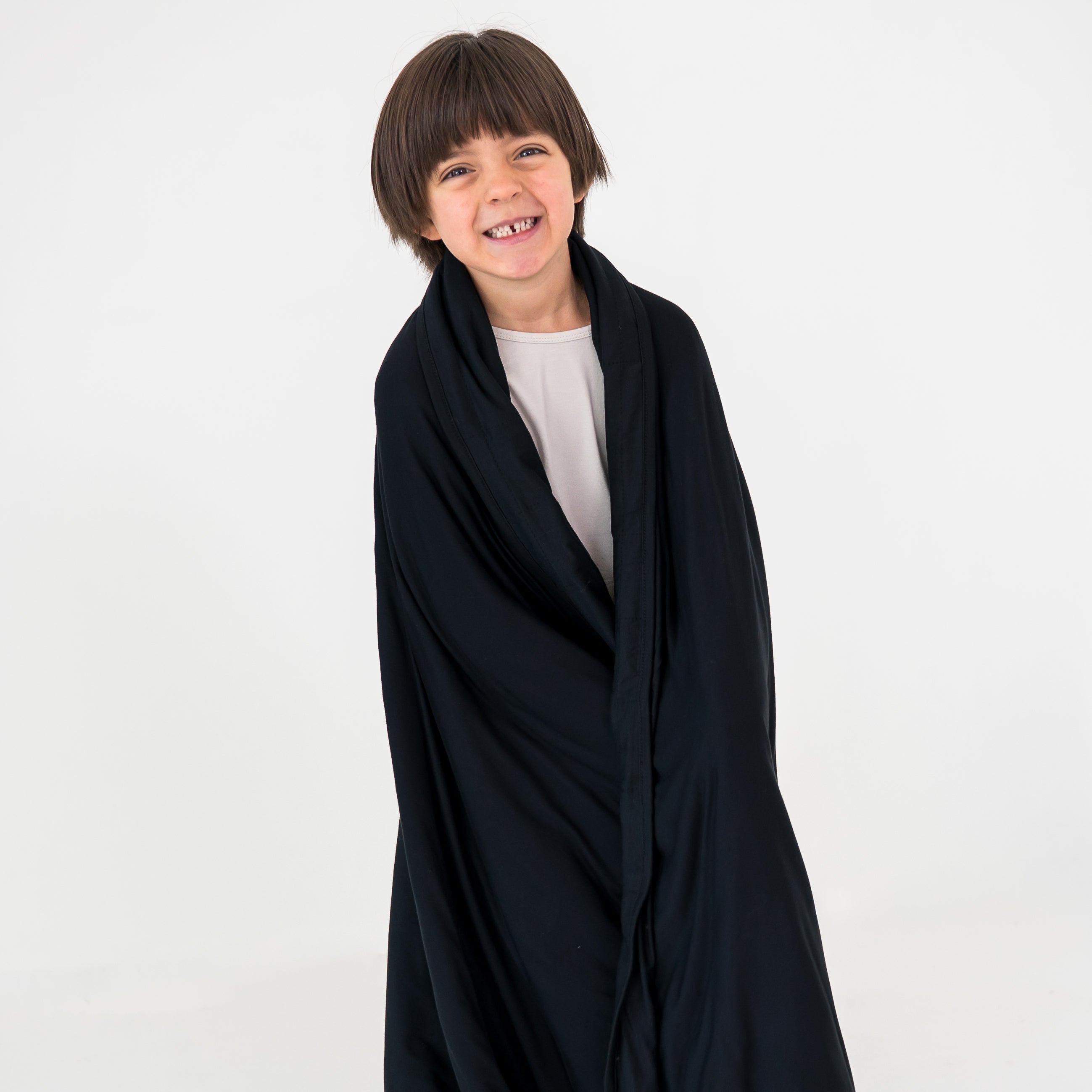 Child wearing a black blanket over a white shirt on a white background
