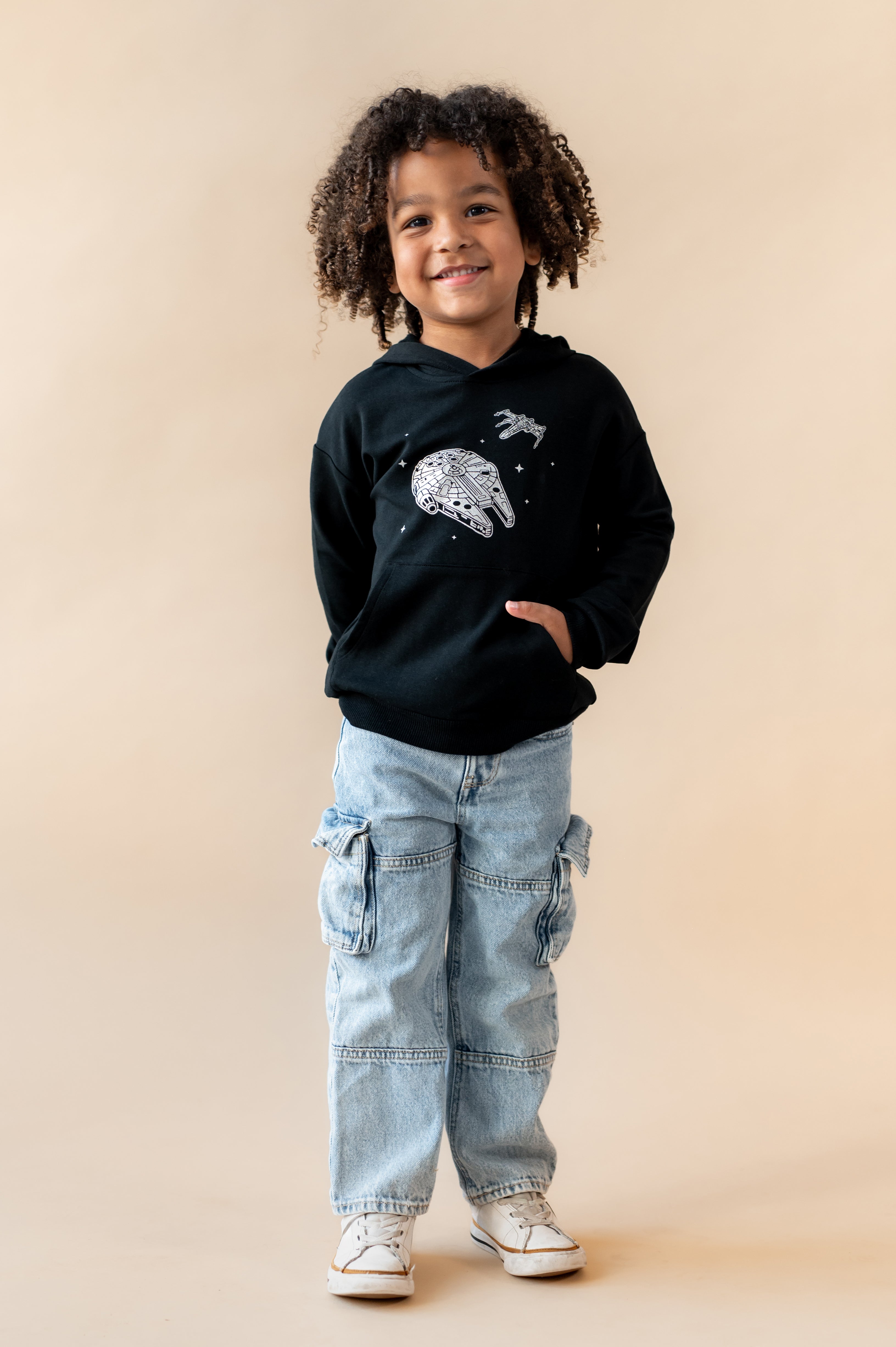 Boy wearing Black Hoodie with Millennium Falcon™ print in center over a blue jeans on a beige background