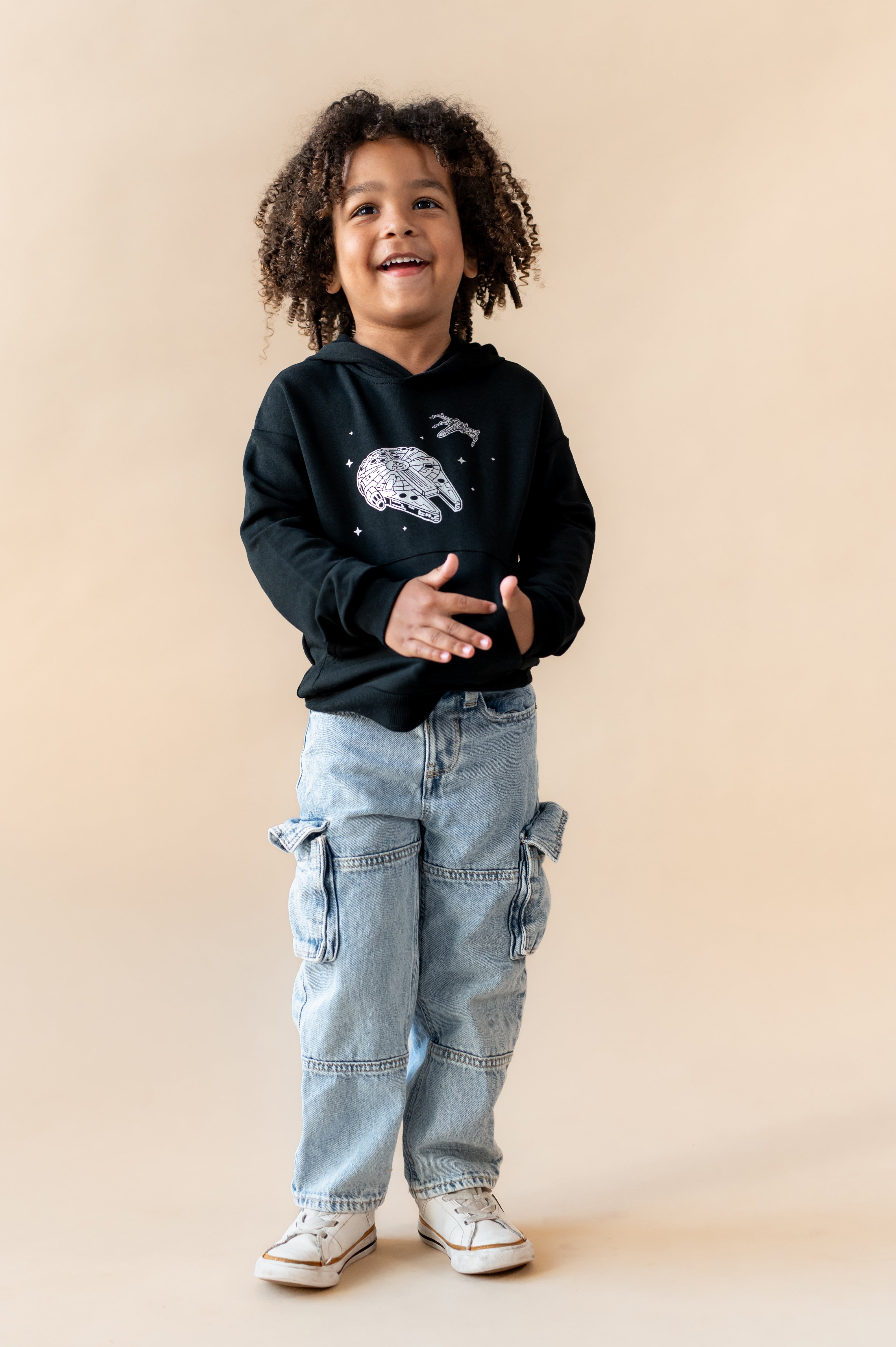 Boy wearing Black Hoodie with Millennium Falcon™ print in center over a blue jeans on a beige background