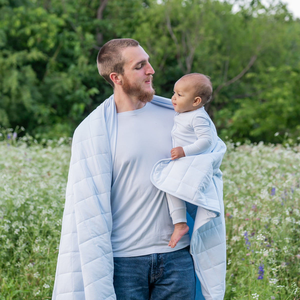 Man in Men's Crew Neck Tee in Mist holding baby wearing matching Mist Romper wrapped in Mist Adult Blanket