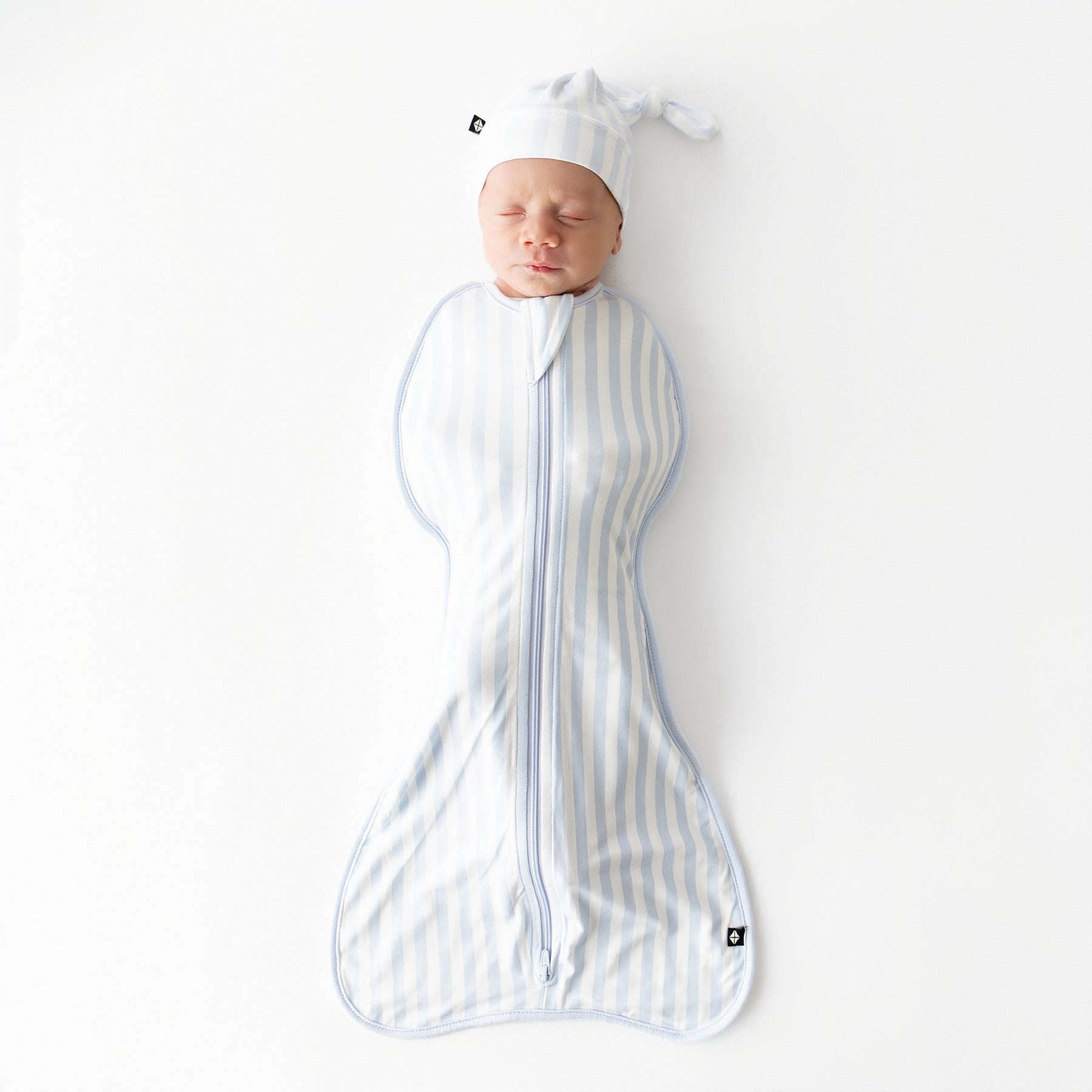 Sleeping newborn laying on a white surface wearing the breathable Swaddle Bag in Small Mist Stripe 0.5 from Kyte Baby