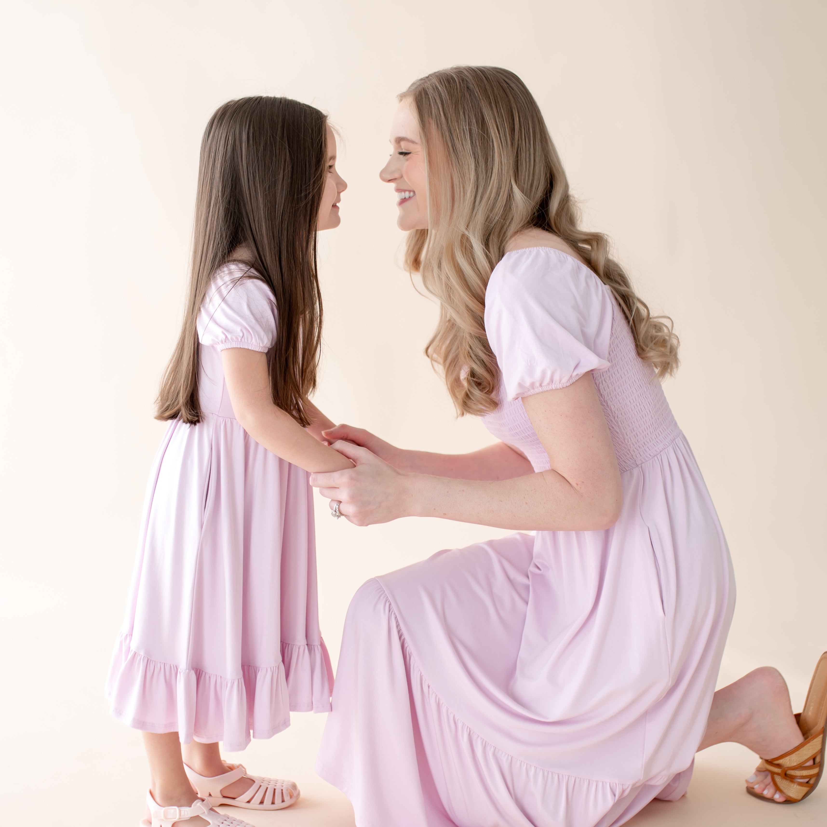 Woman and young girl in matching purple dresses holding hands against a plain background
