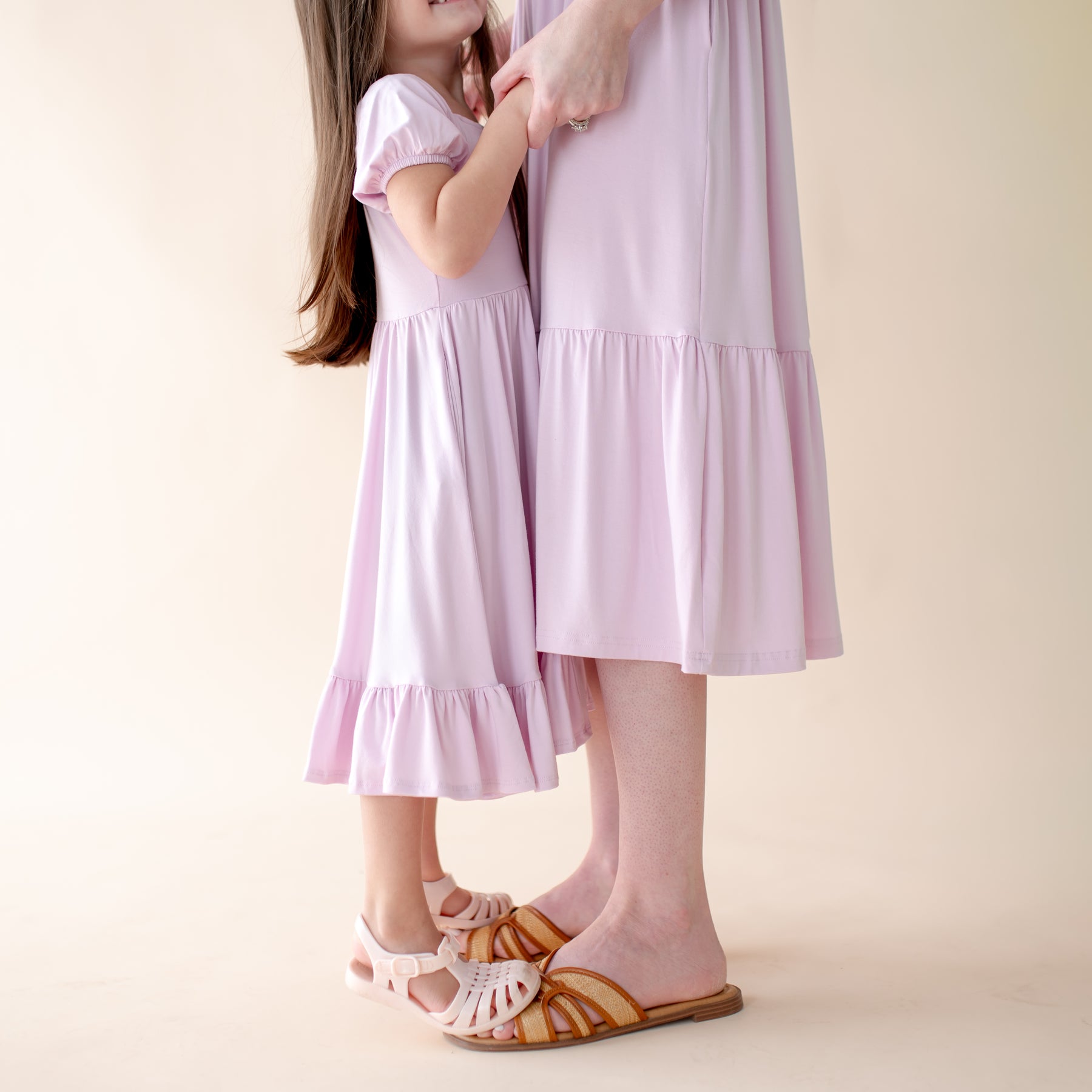 Two people wearing matching light purple dresses on a plain background
