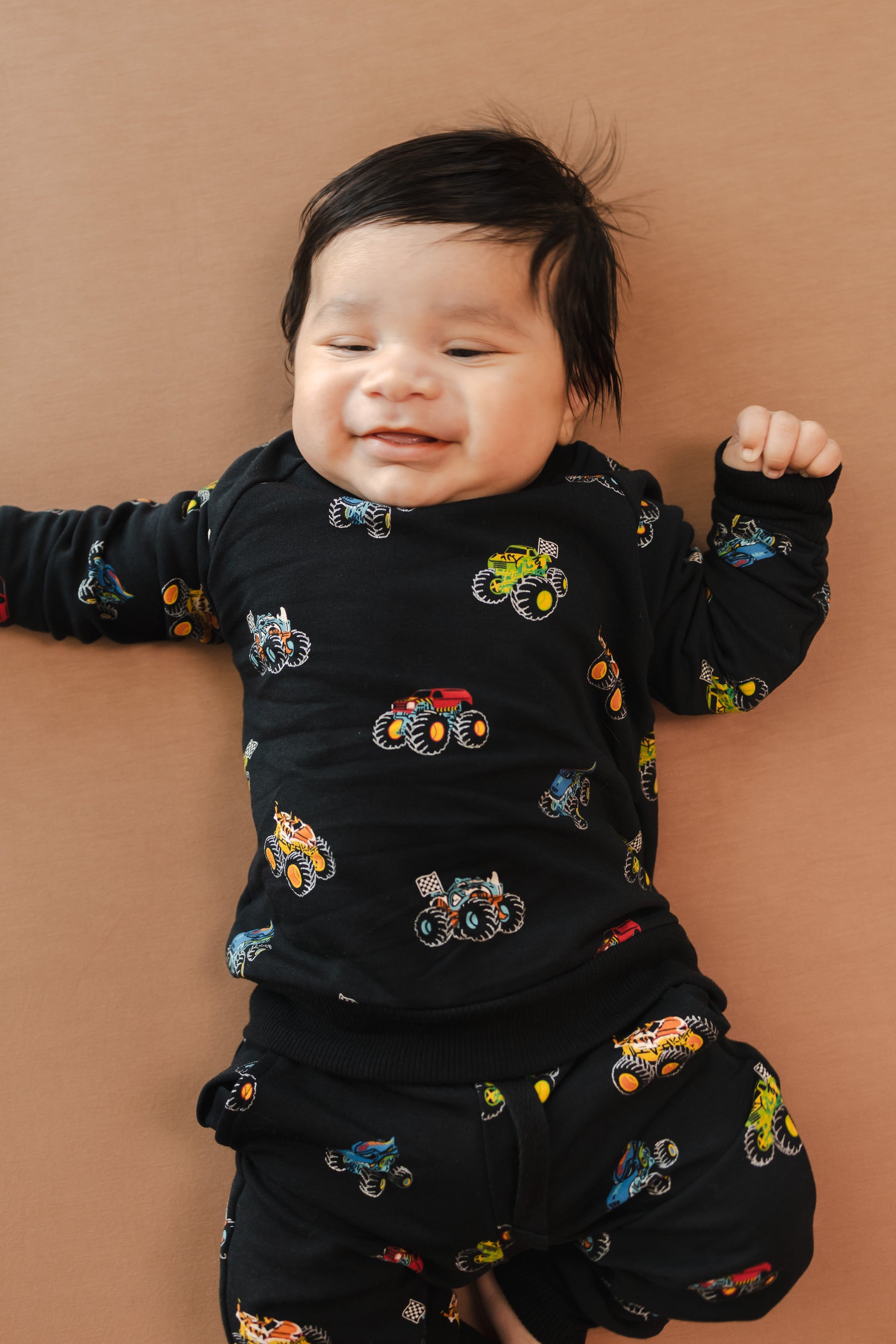 Baby wearing black Long Sleeve Jogger Set in Monster Truck print on beige background