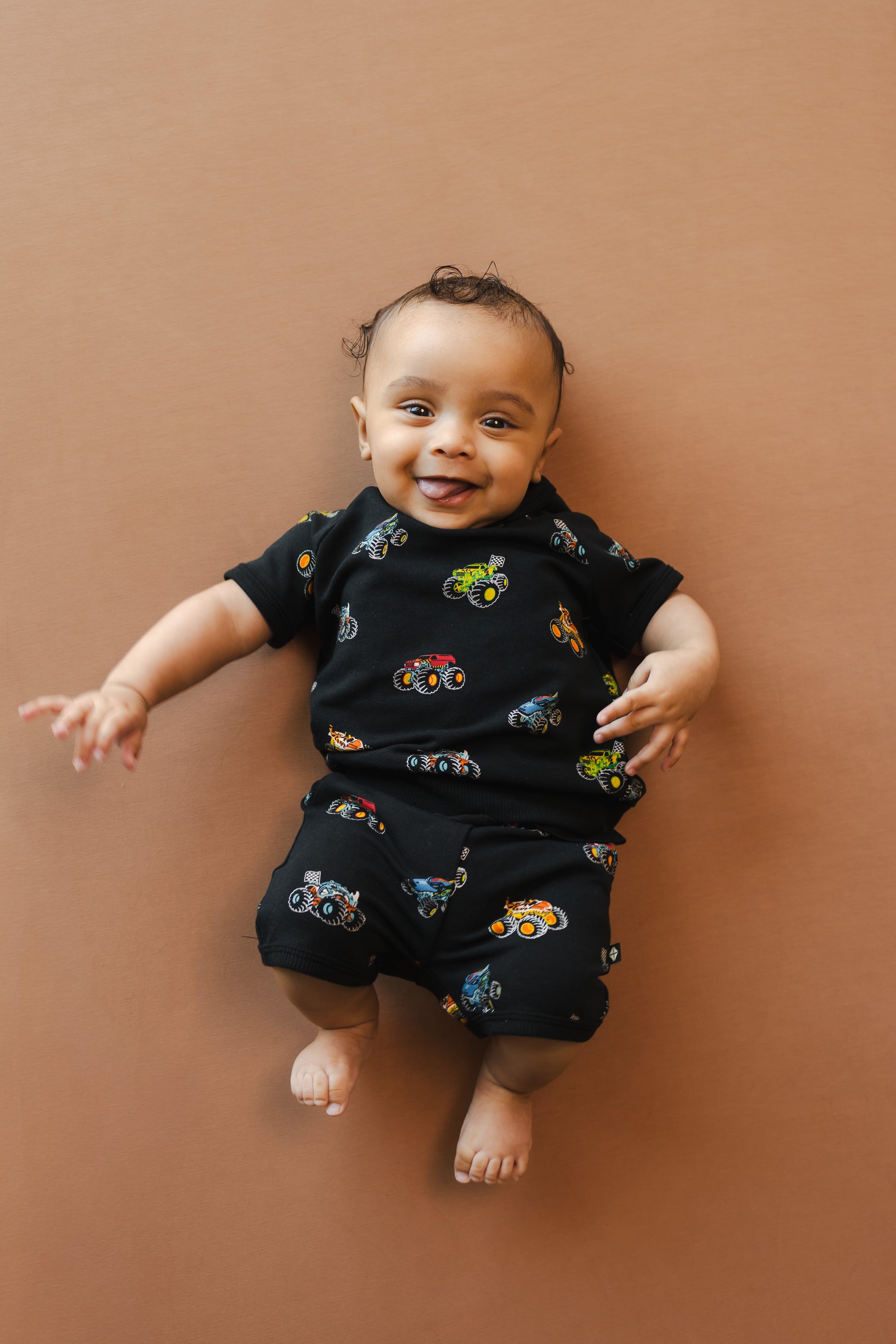 Baby wearing Black Short Sleeve Jogger Set in Monster Truck print on beige background