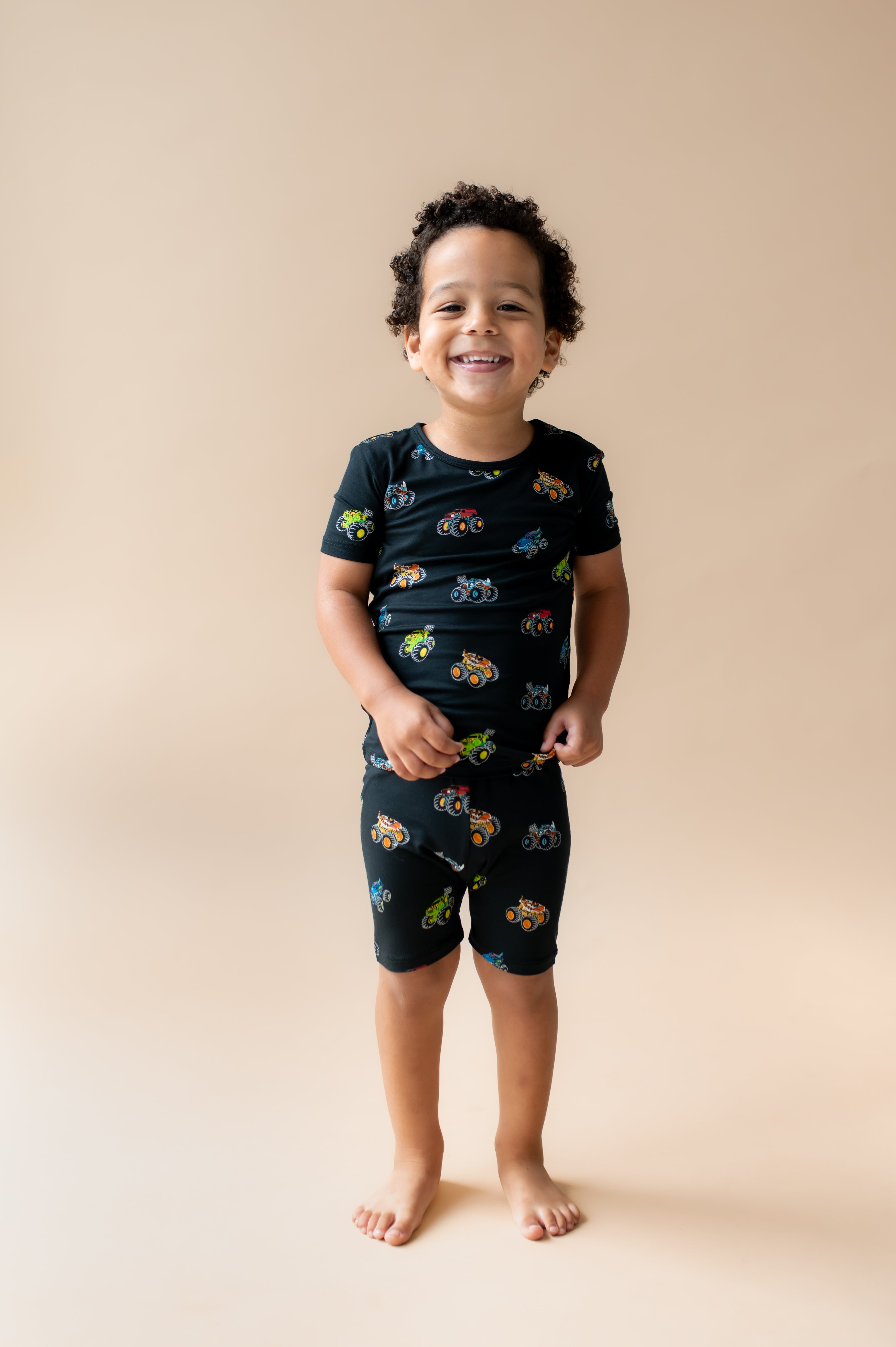Boy wearing Black Short Sleeve Pajamas in Monster Truck print on beige background
