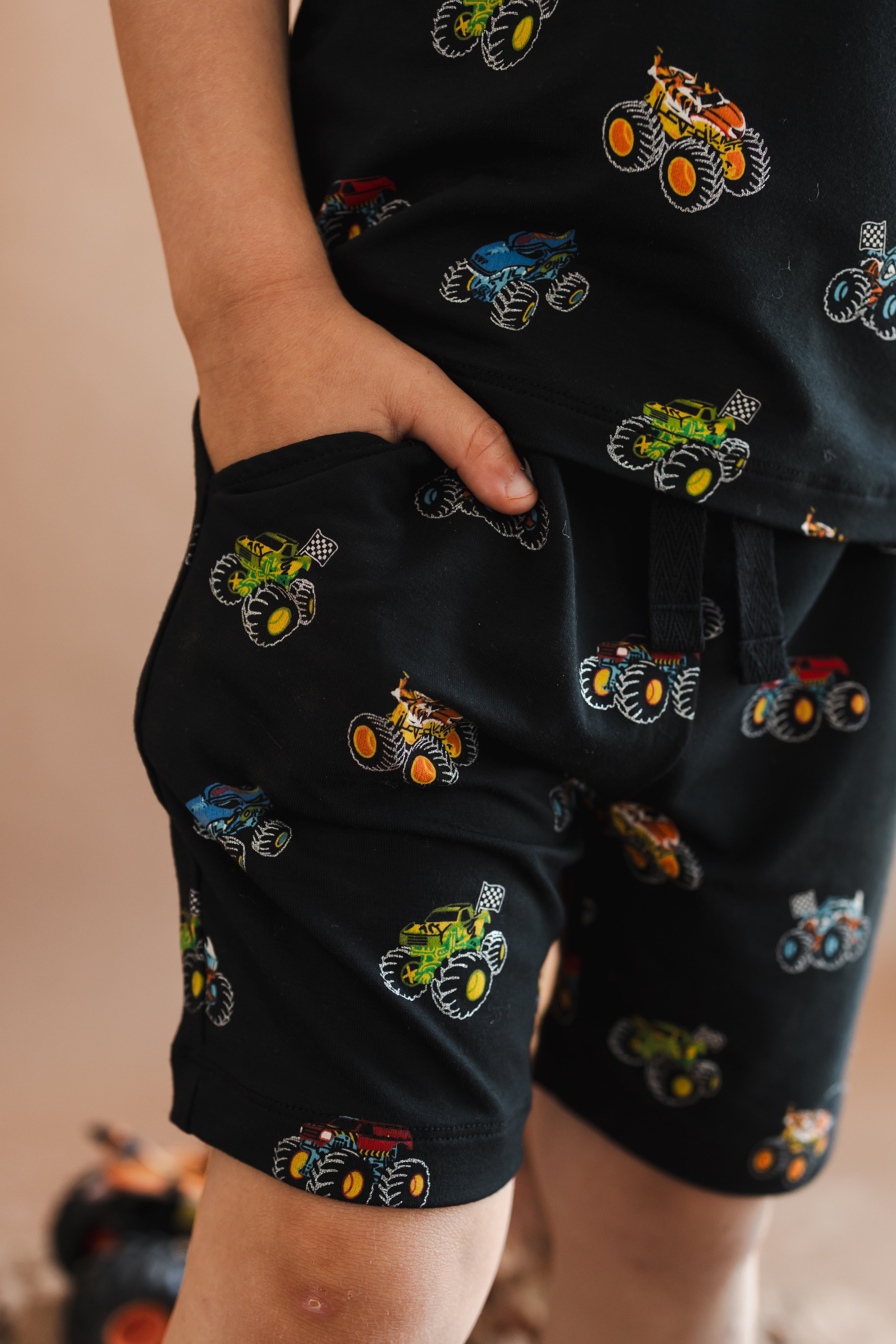Boy wearing Black drawstring short in Monster Truck print with pocket on beige background