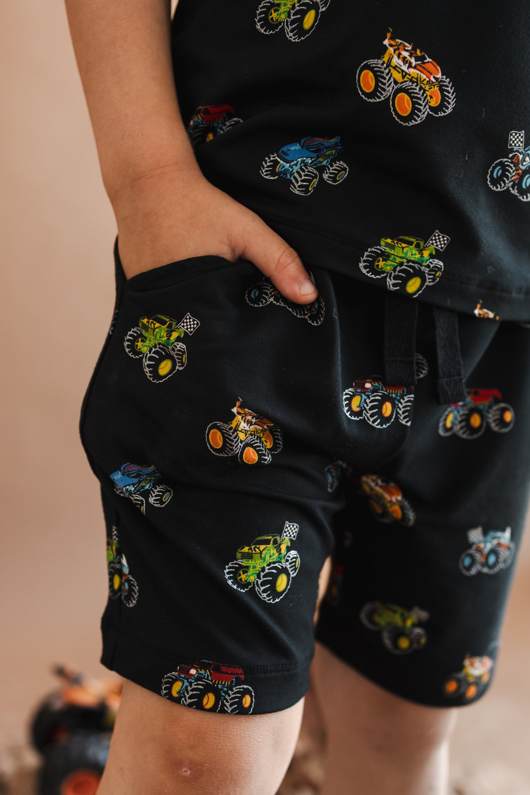 Boy wearing Black drawstring short in Monster Truck print with pocket on beige background
