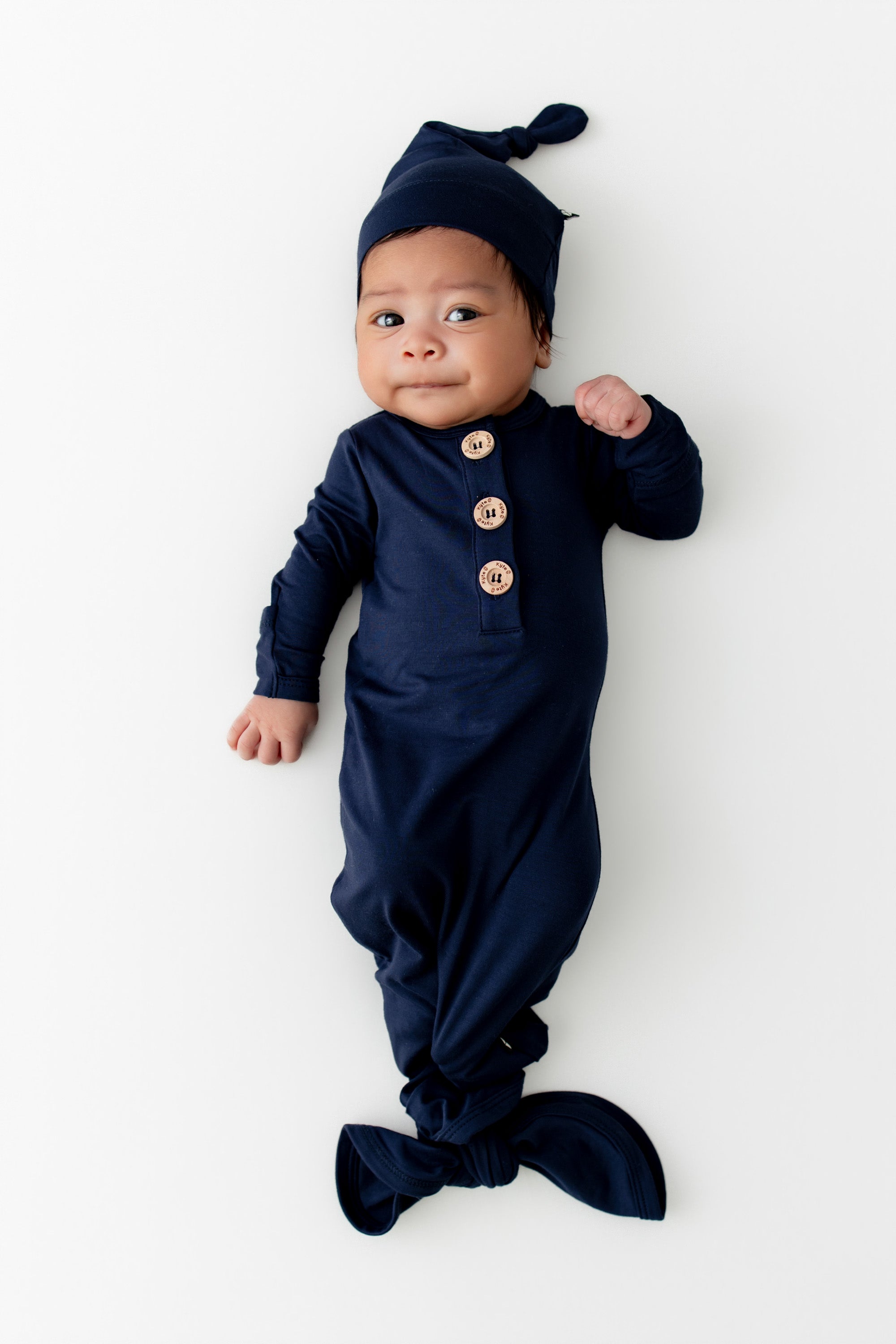 Baby wearing a navy blue outfit with buttons and matching hat on a white background