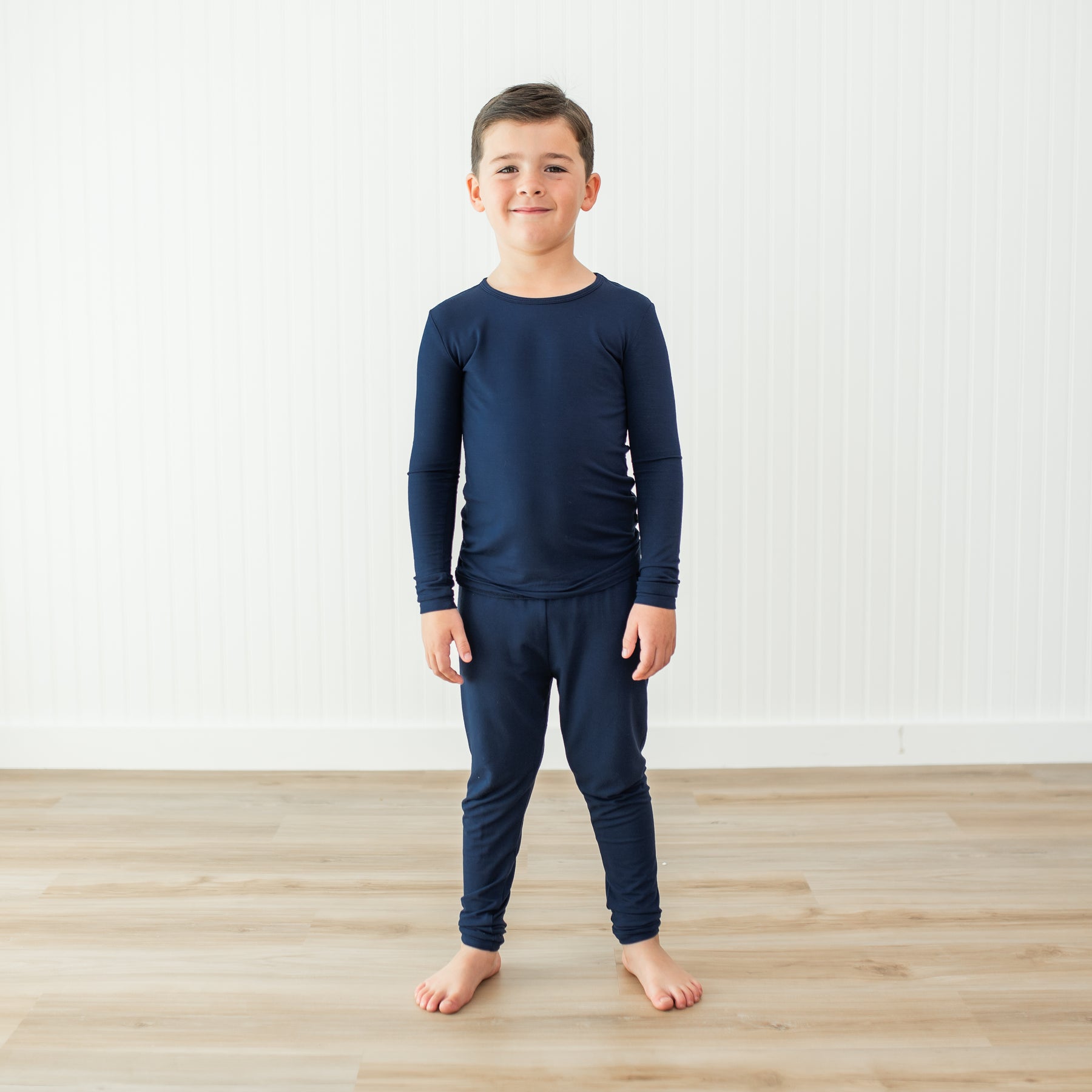 Child wearing a navy blue long-sleeve shirt and pant pajama set on a light wooden floor.