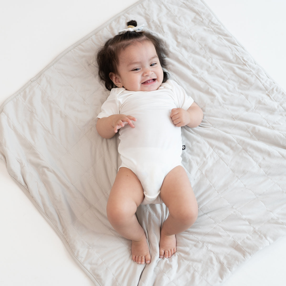 Baby in cloud bodysuit laying on Baby Blanket in Oat 1.0