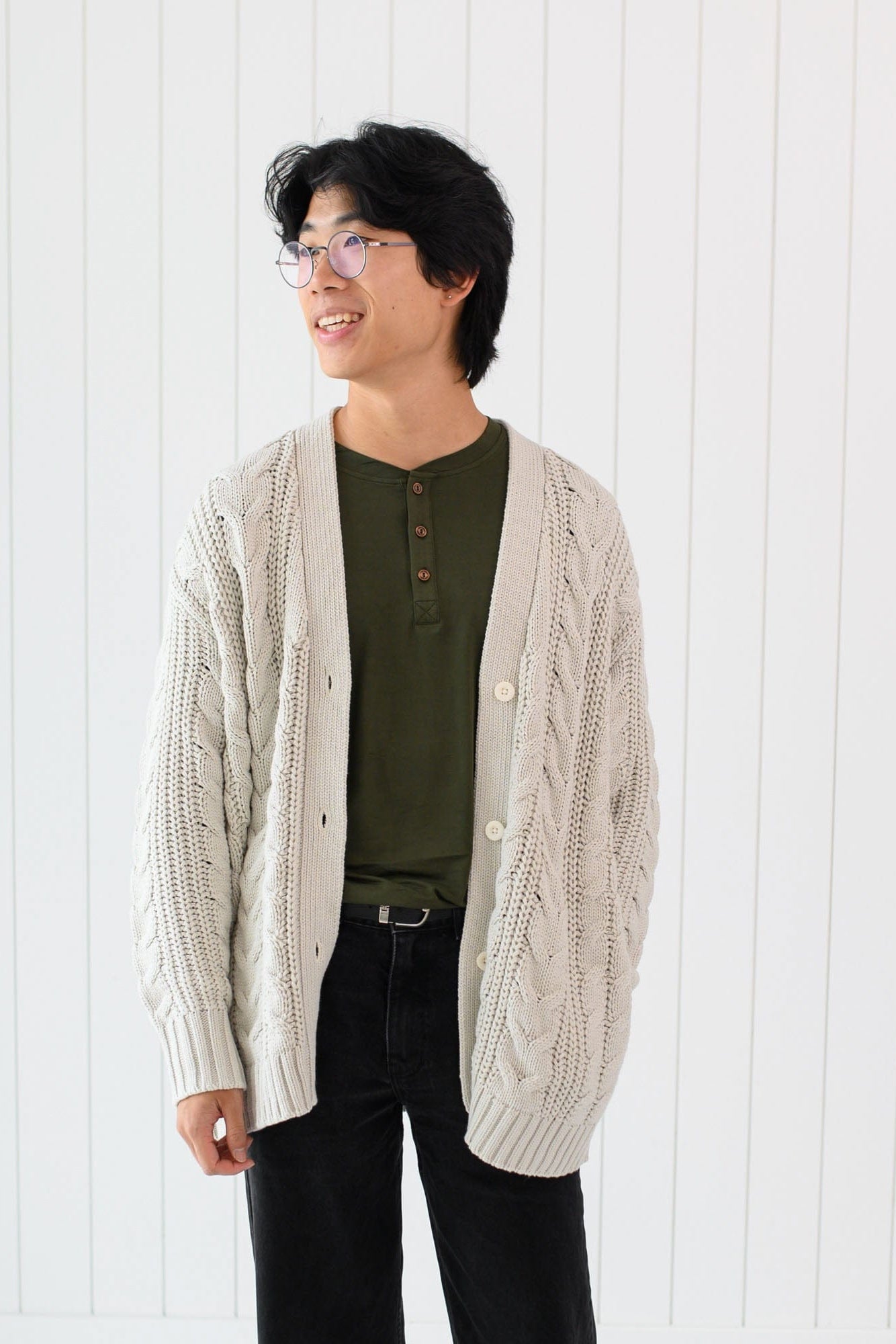 Male model wearing the Cable Knit Adult Cardigan in Oat with a dark olive green shirt and black pants