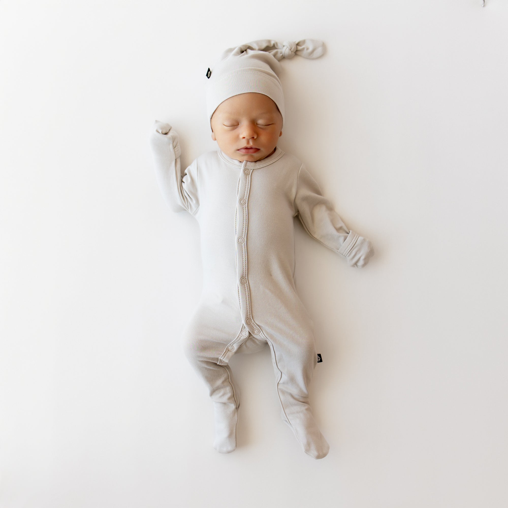 Baby in a snap footie in a creamy light grey with matching knotted cap