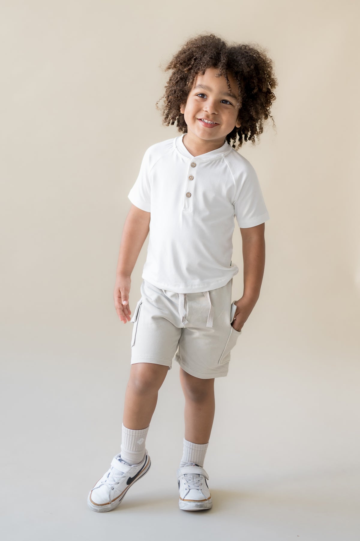 Young boy modeling the Cargo Short in Oat paired with a white short sleeve henley tee