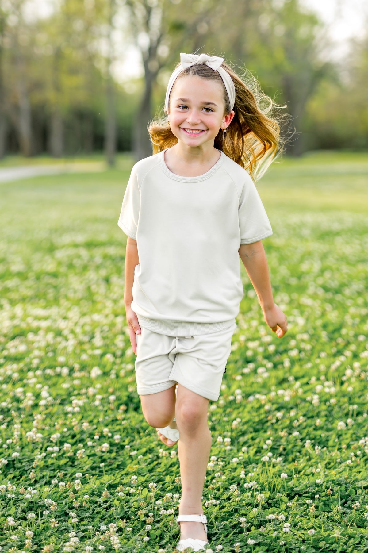 Young girl walking through a grass field wearing the Short Sleeve Jogger Set in Oat