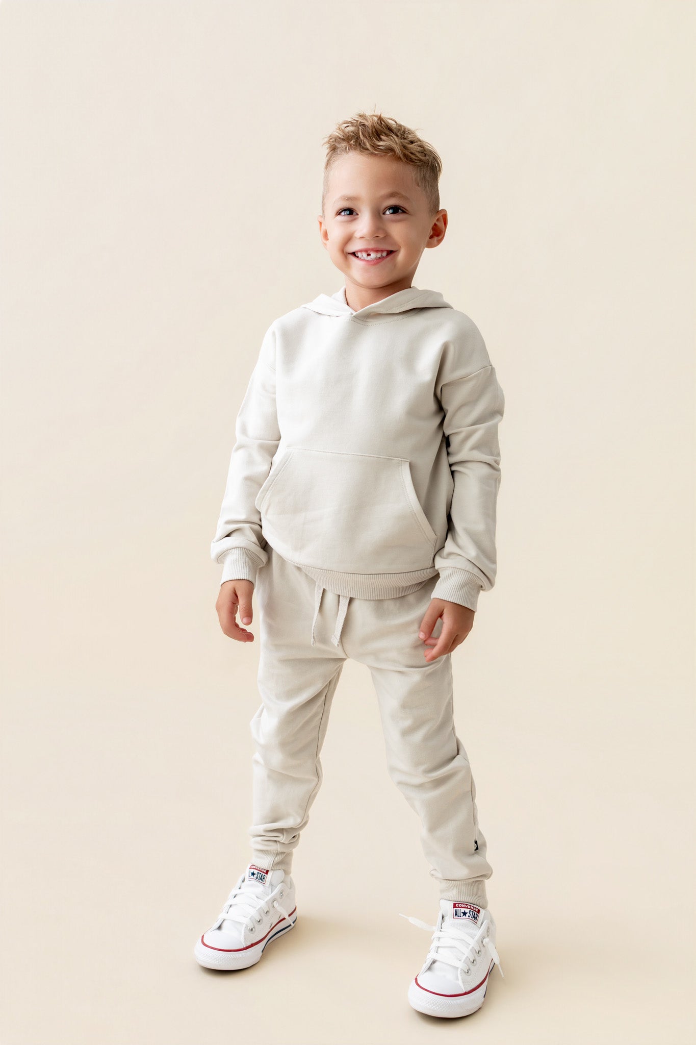 Boy posing in Hoodie in Oat color over similar color jogger pants on a beige background