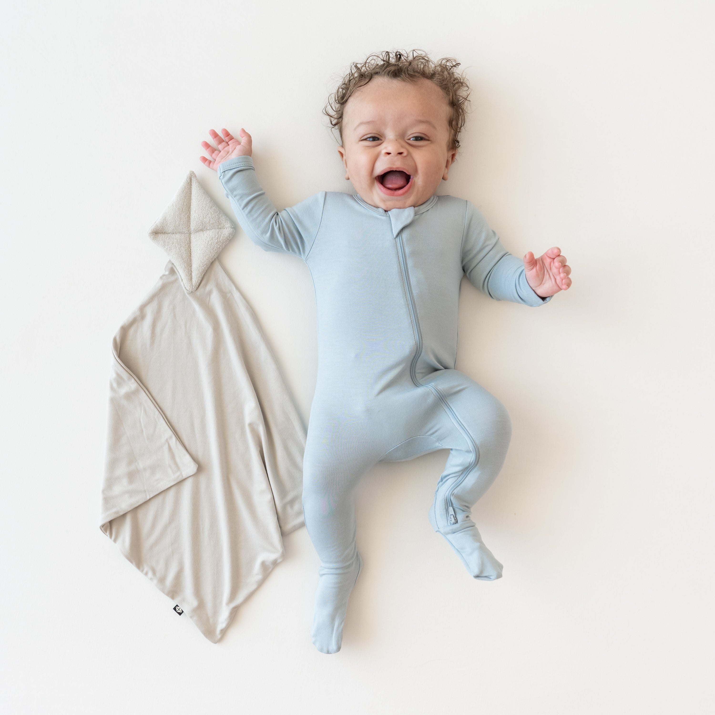 Baby in fog zippered footie laying next to Kite Lovey in Oat