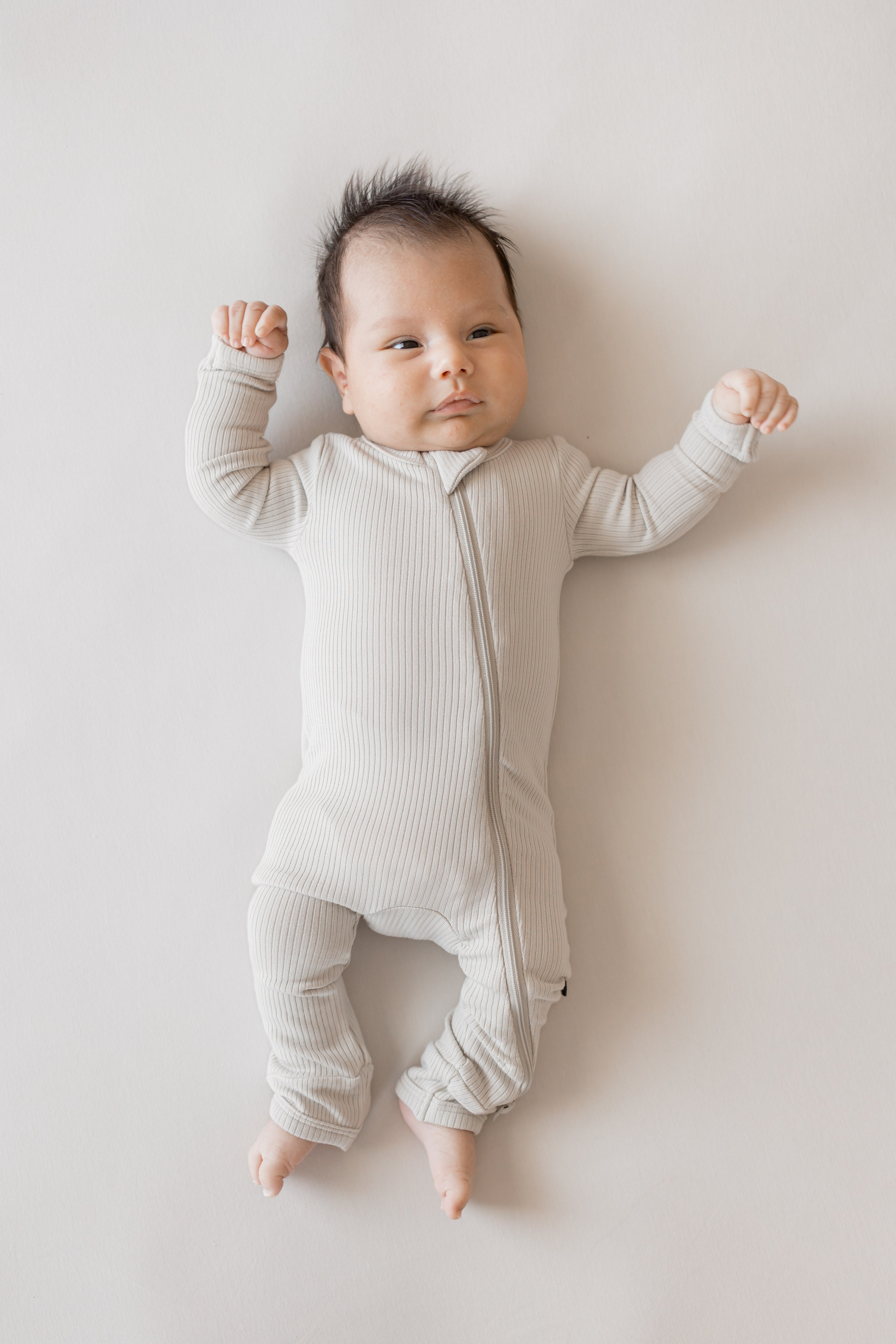 Baby wearing Ribbed Zipper Romper in Oat color on a beige background