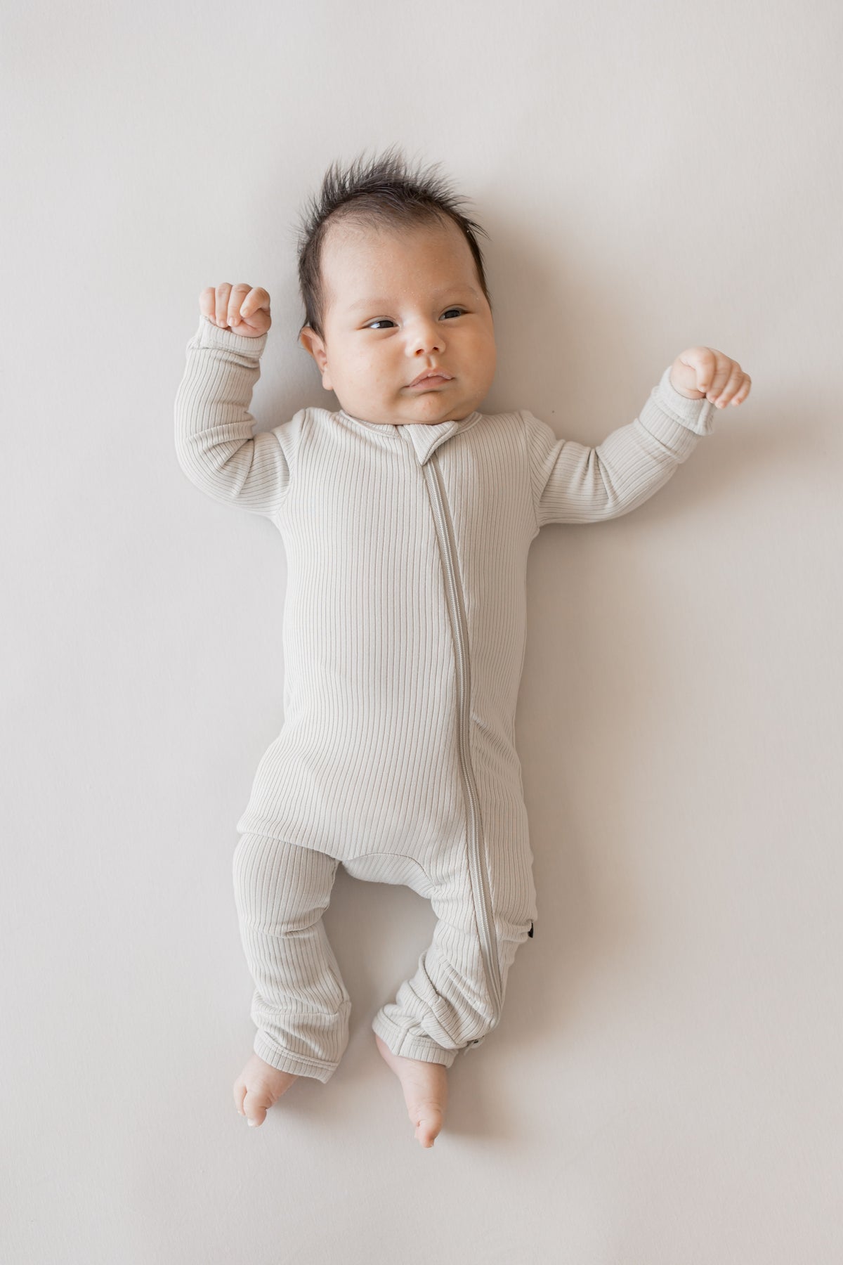 Baby wearing Ribbed Zipper Romper in Oat color on a beige background