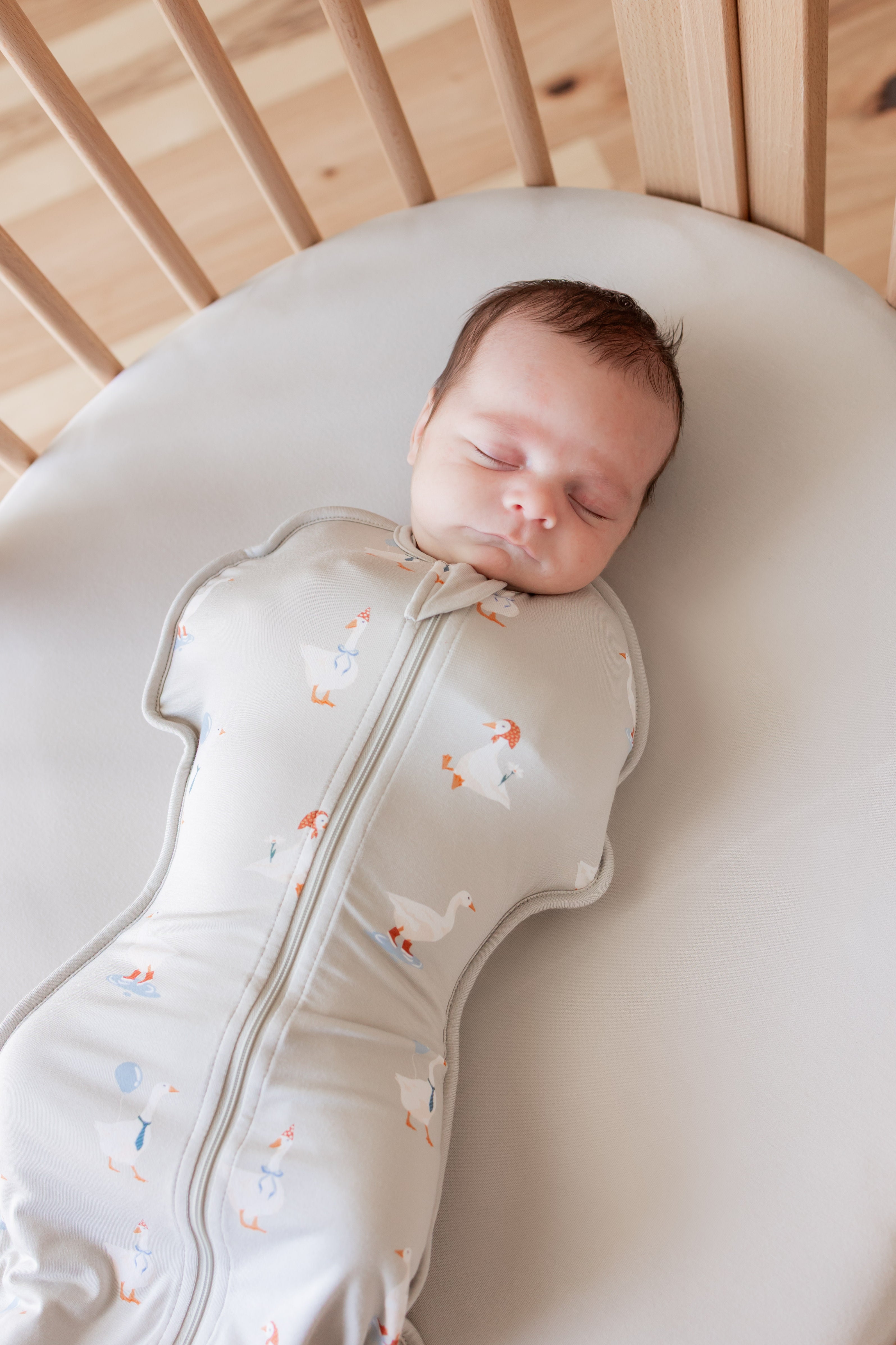 Baby sleeping in crib wearing Swaddle Bag in Oat Silly Goose 0.5 print over oat color sheet