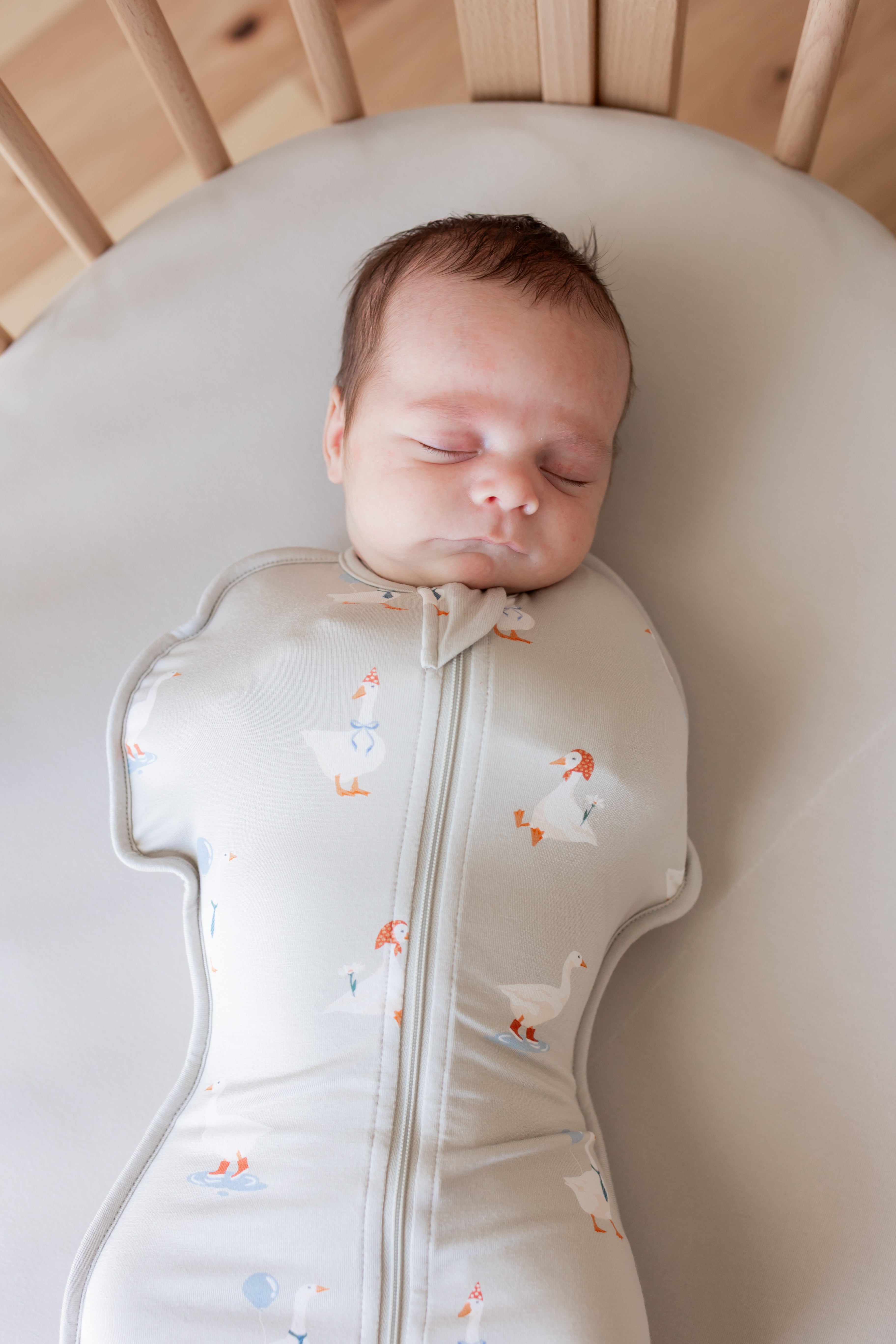 Baby sleeping in crib wearing Swaddle Bag in Oat Silly Goose 0.5 print over oat color sheet