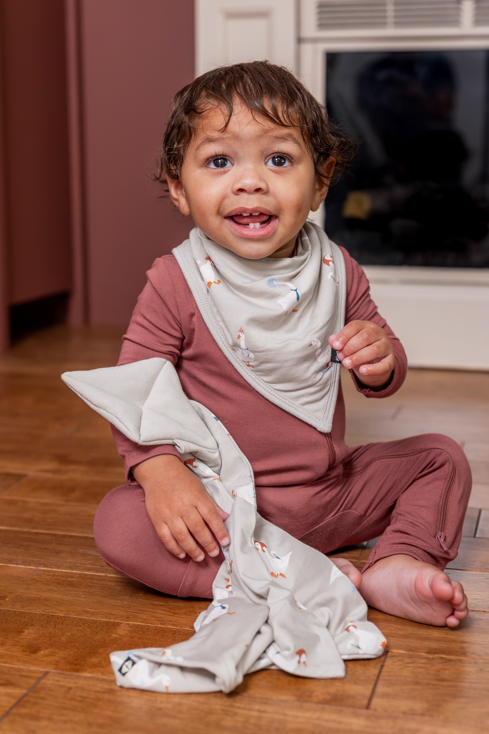 Toddler wearing Bib in Oat Silly Goose print over ember color zippered romper holding Kite lovey in oat silly goose print