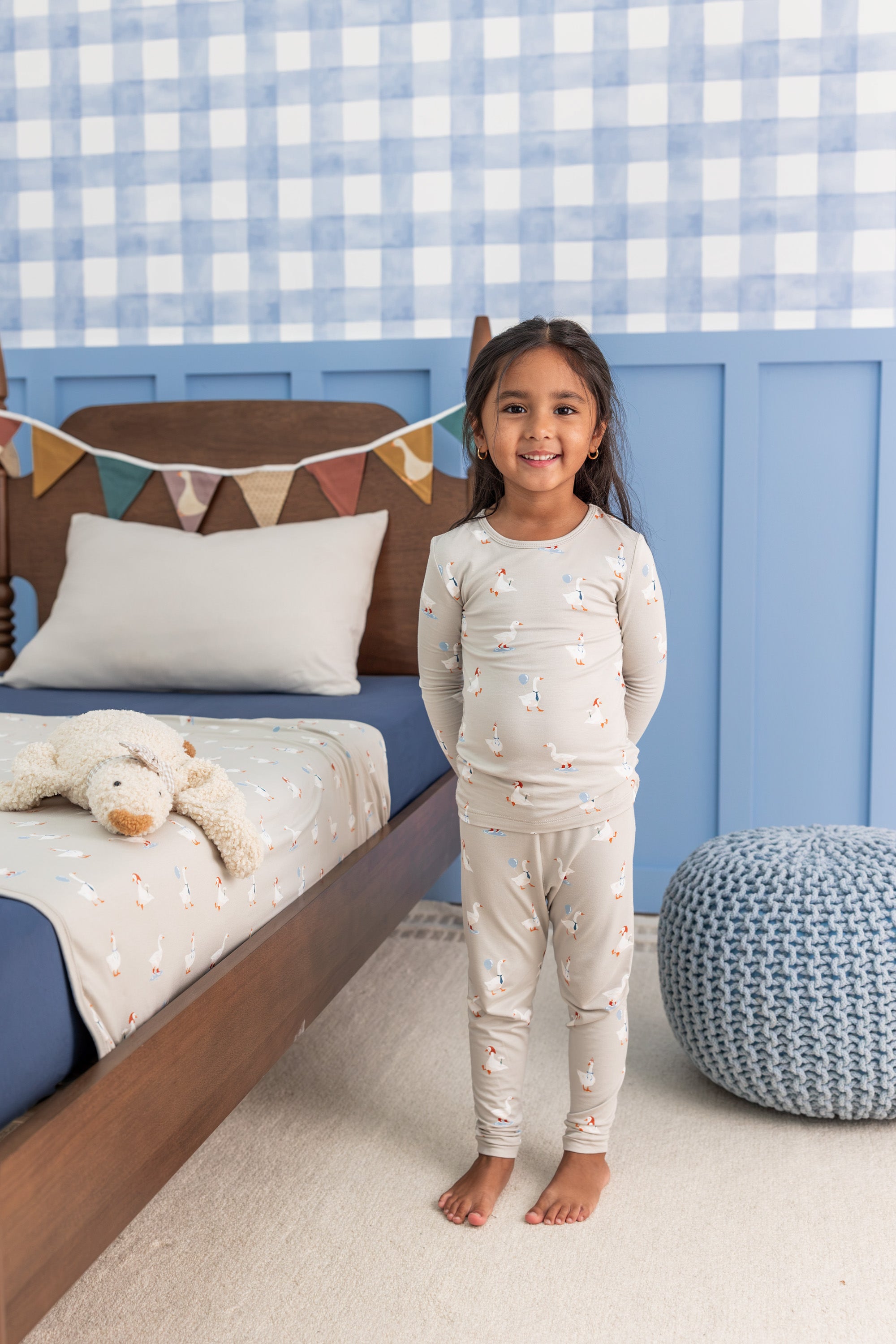 Girl wearing Long Sleeve Pajamas in Oat Silly Goose print standing beside a bed