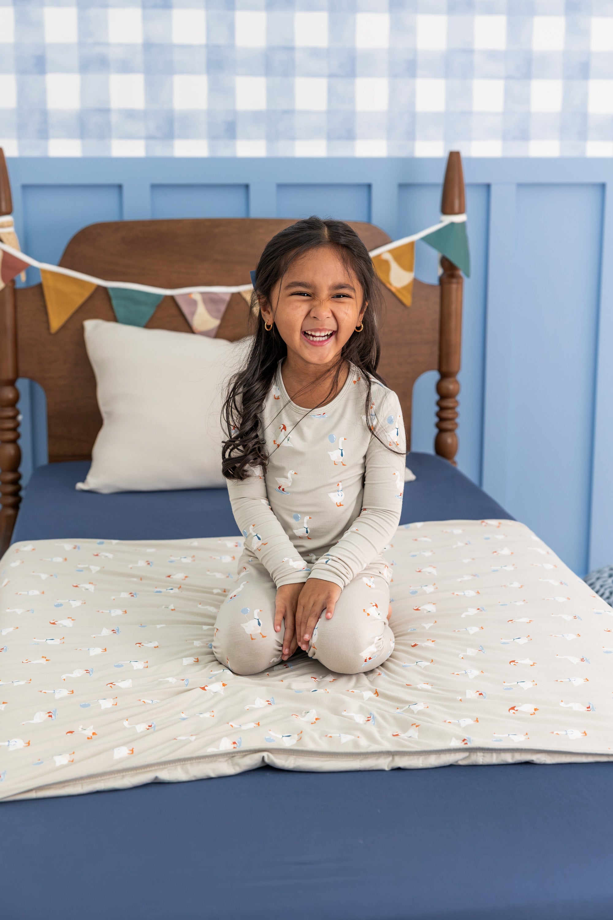 Girl wearing Long Sleeve Pajamas in Oat Silly Goose print smiling on a bed