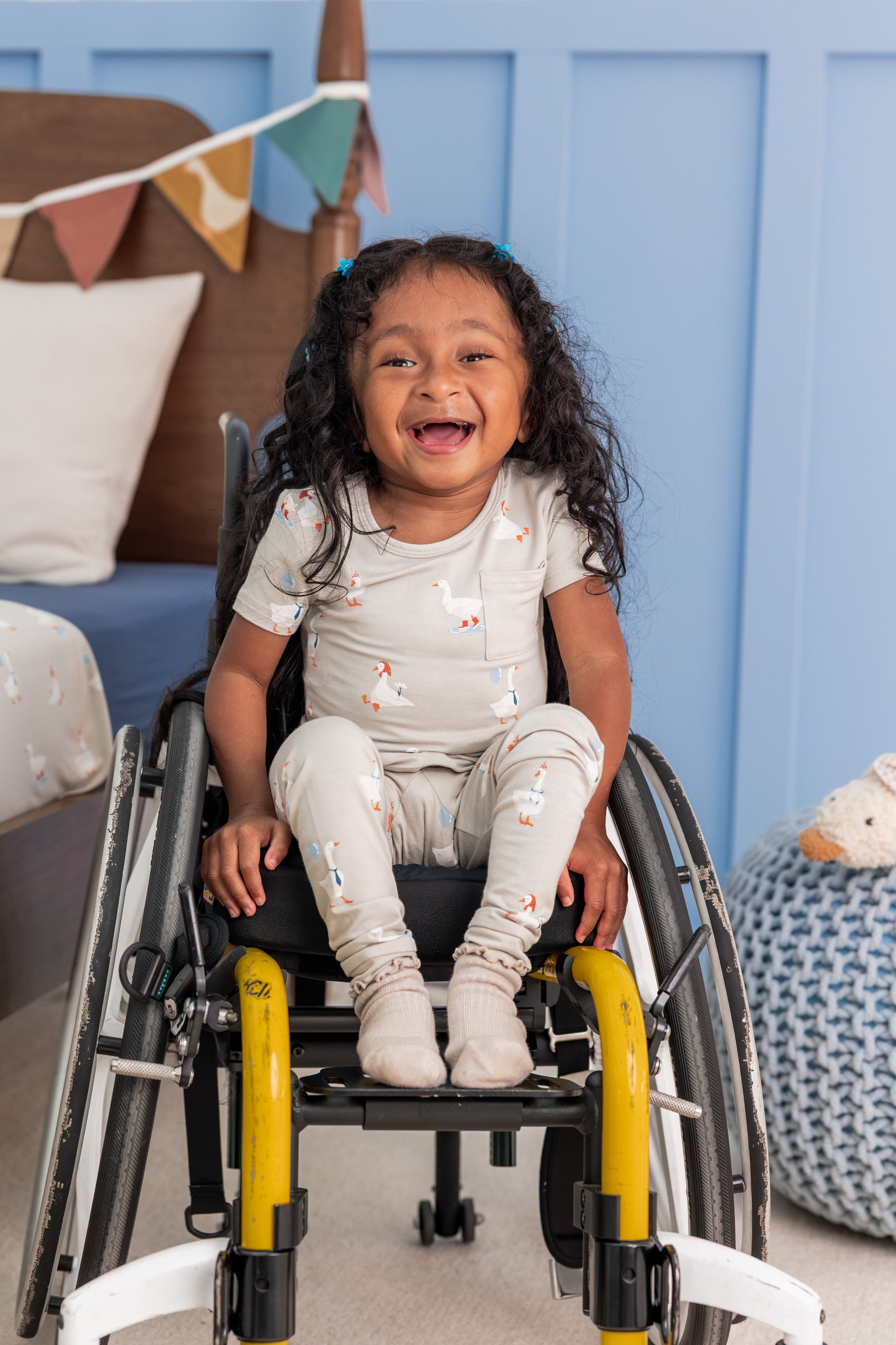 Toddler wearing Short Sleeve with Pants Pajamas in Oat Silly Goose print sitting on a wheel chair