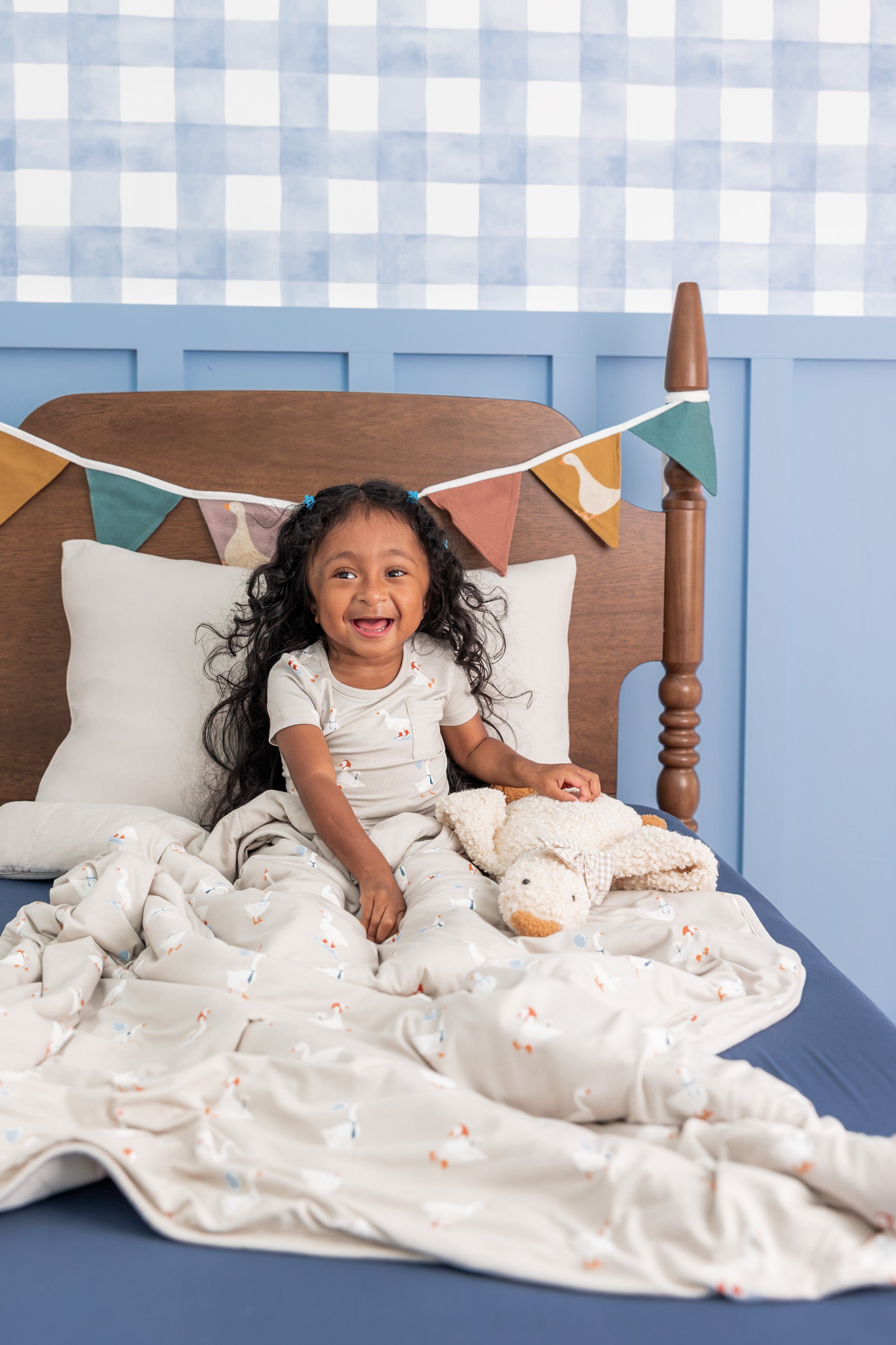 Toddler wearing Short Sleeve with Pants Pajamas in Oat Silly Goose print sitting on a bed with similar print blanket and silly goose stuff toy