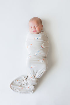 Baby wrapped in Swaddle Blanket in Oat Silly Goose print on an oat color background