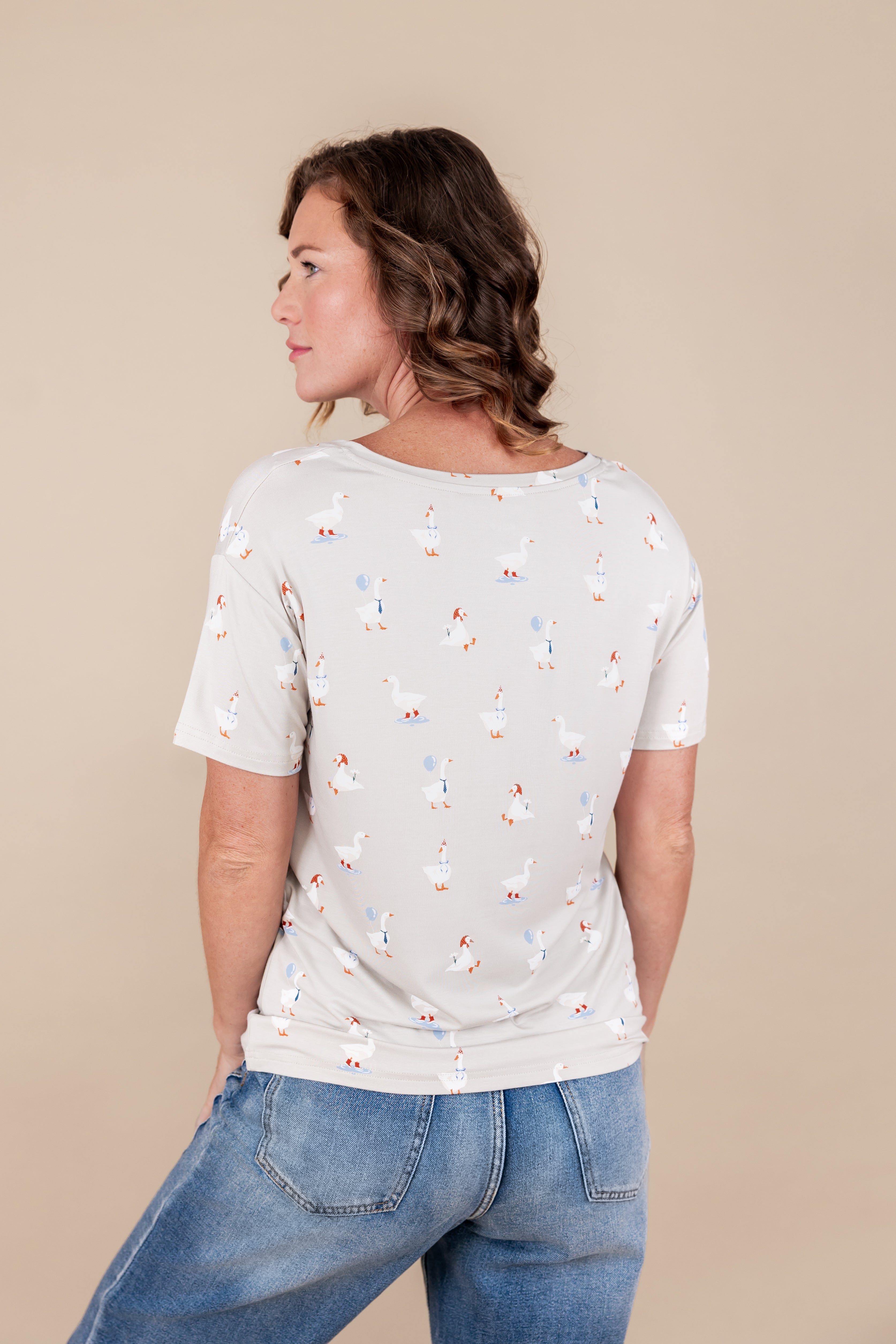 Back side of Modal wearing Women's Oversized V-Neck in Oat Silly Goose print over blue jeans on a beige background