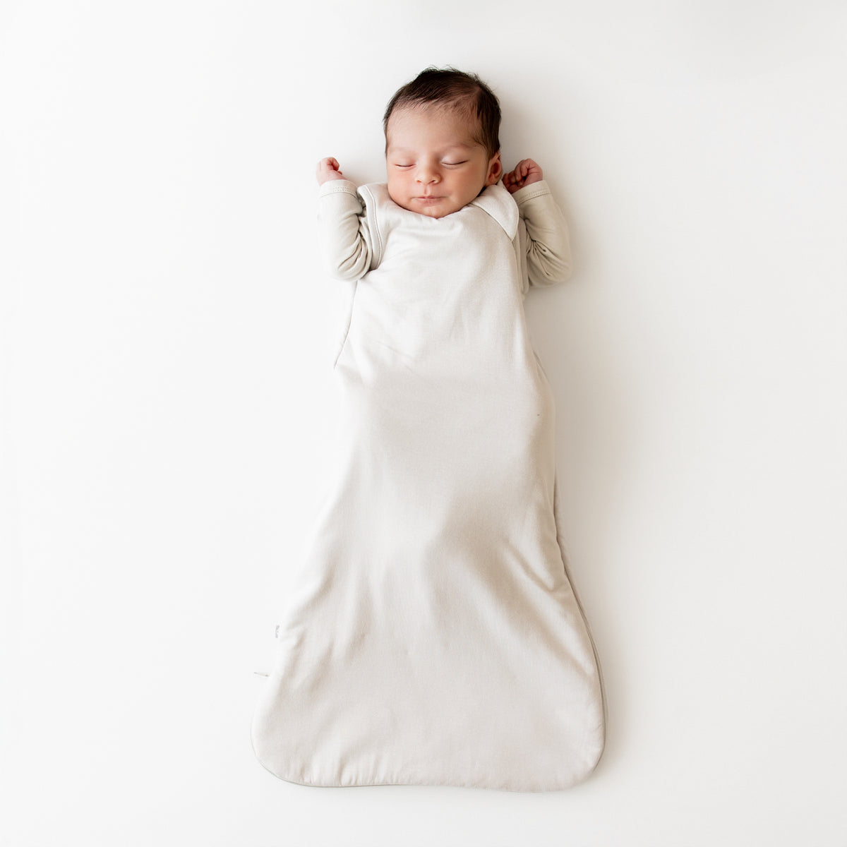 Newborn baby sleeping in a creamy grey sleep bag on a light background