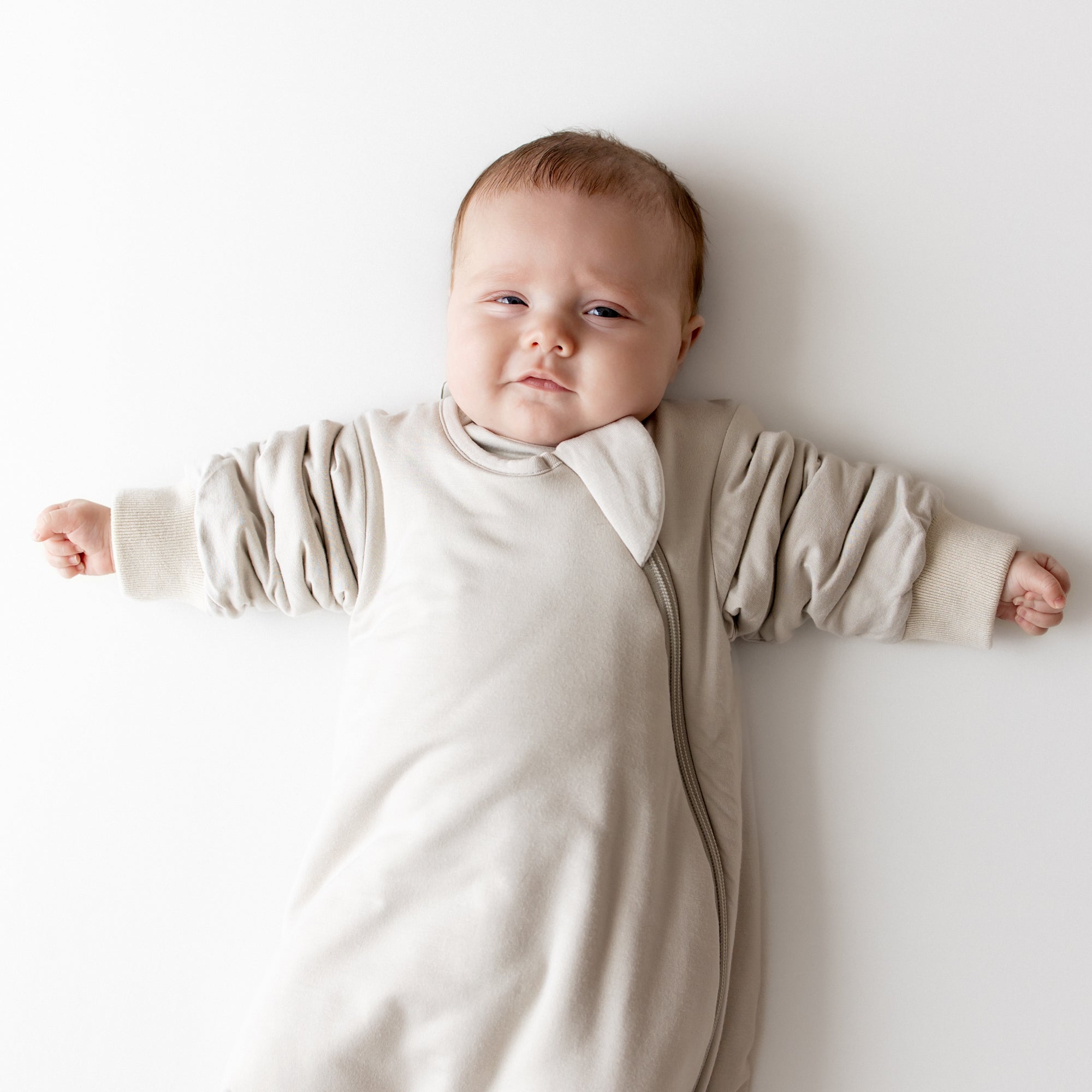 Baby in oat slumber bag on a neutral backdrop